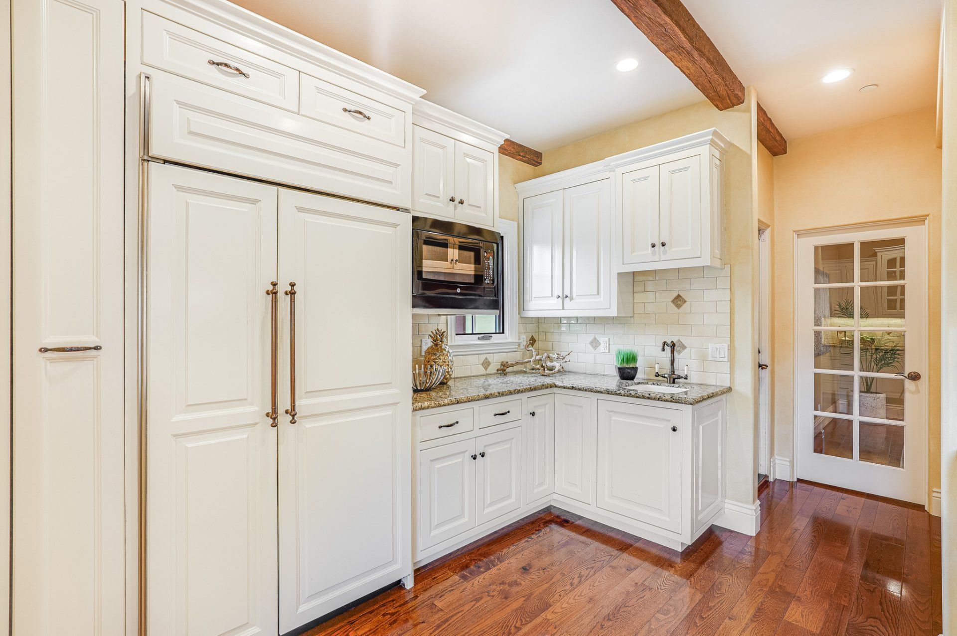 A kitchen with white cabinets , hardwood floors , a refrigerator and a microwave.