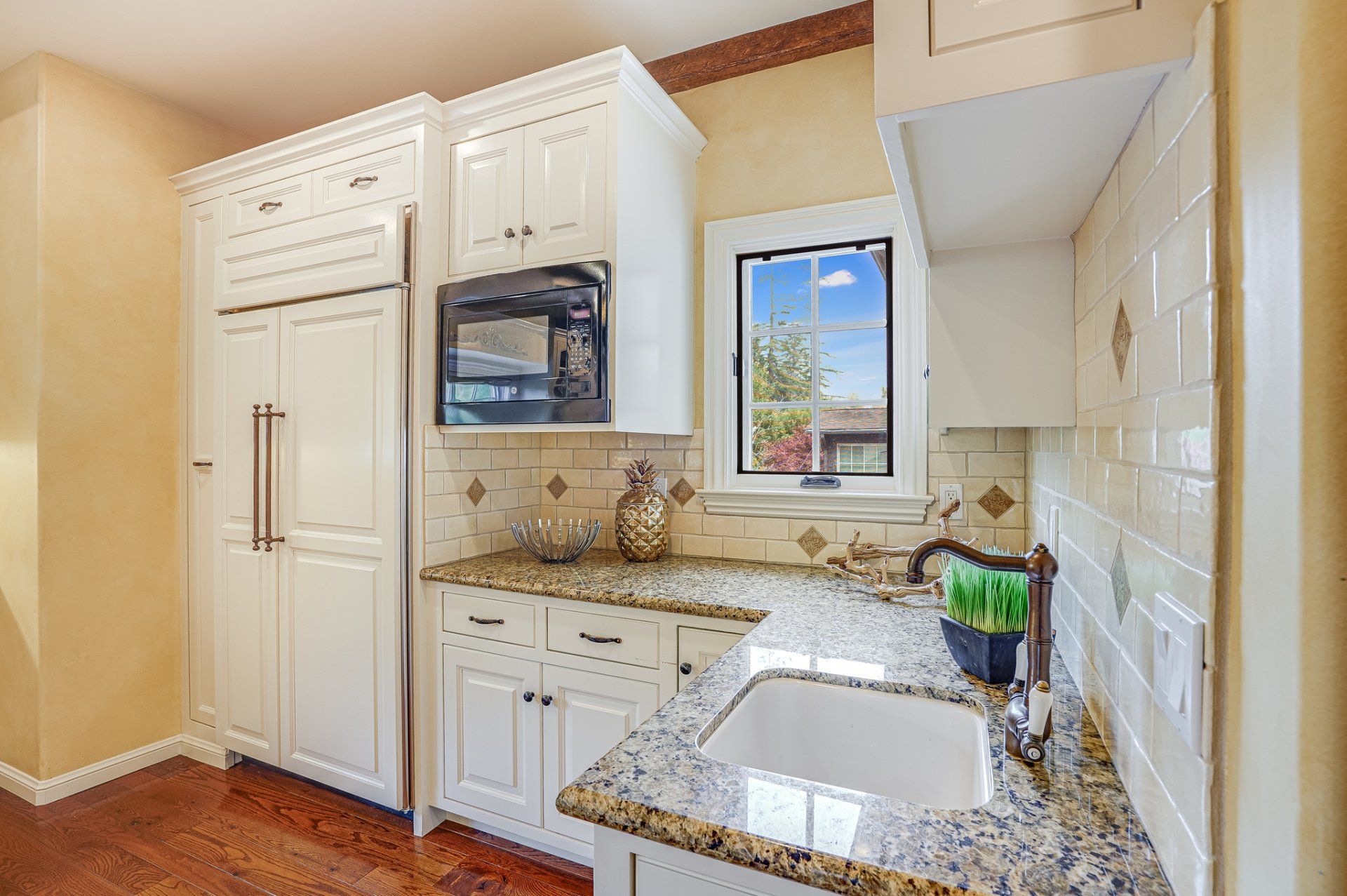 A kitchen with white cabinets , granite counter tops , a sink and a microwave.