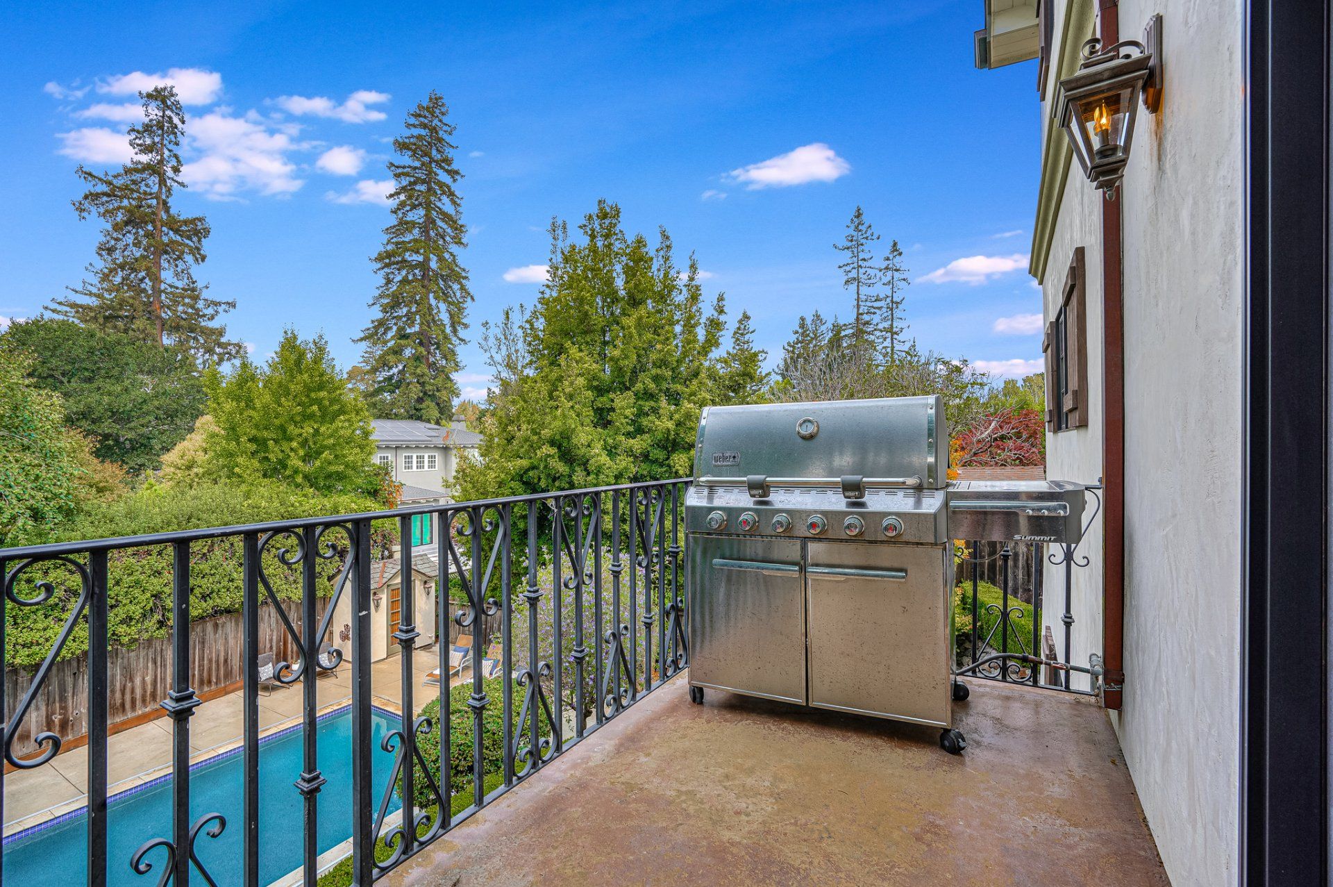 A balcony with a grill and a pool in the background.