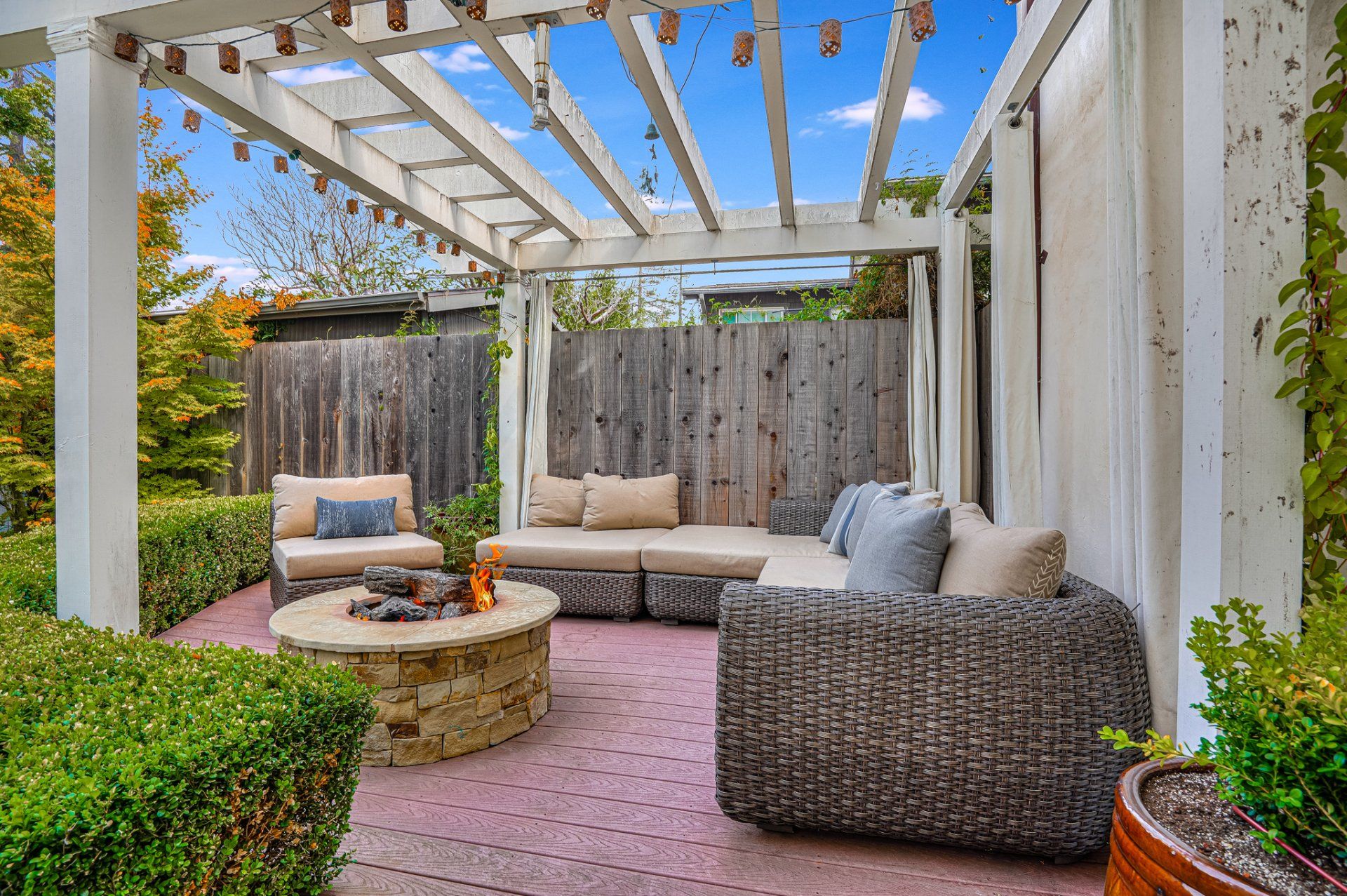A patio with a pergola , couch , chairs and a fire pit.