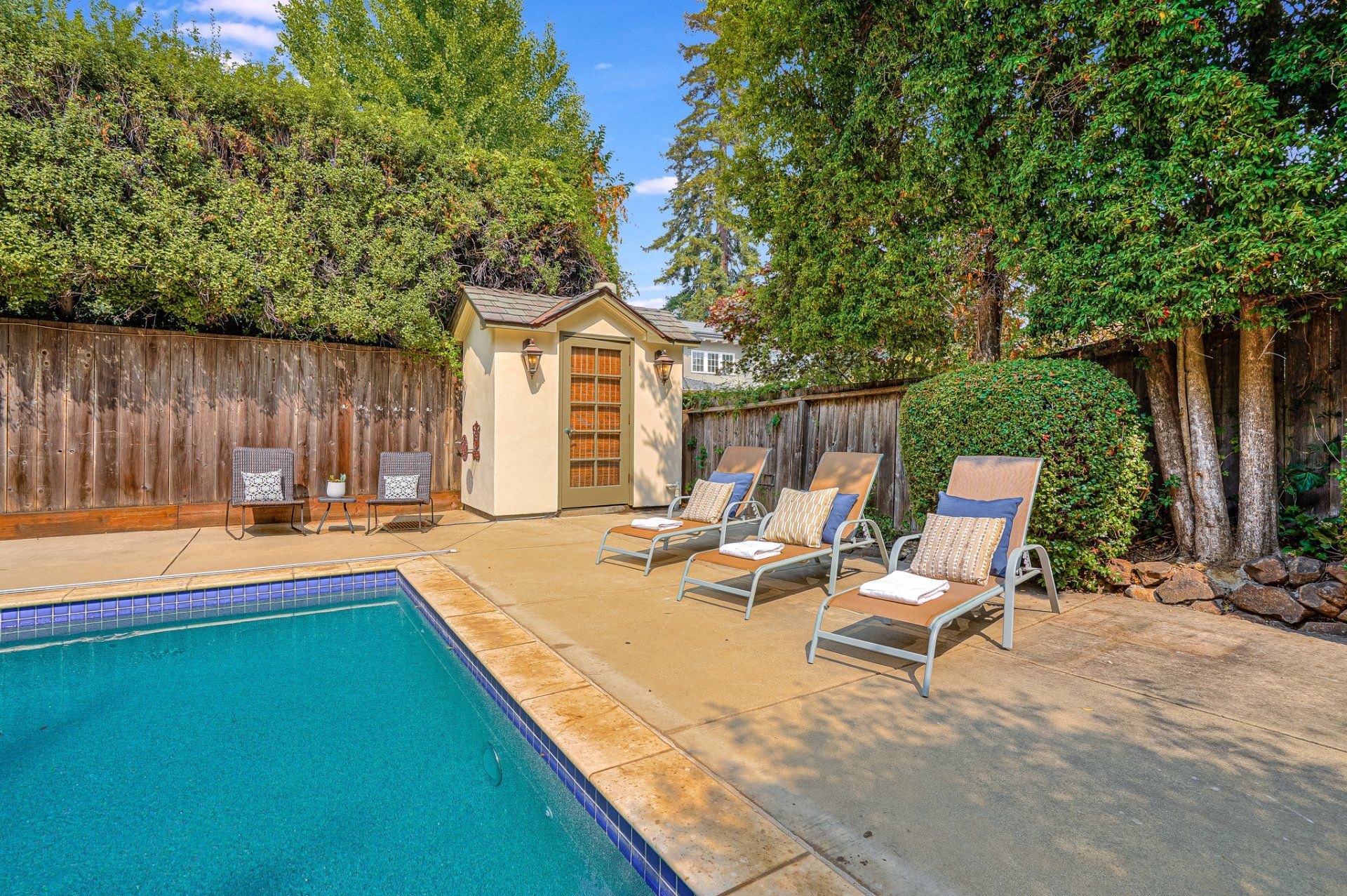 Backyard with pool, lounge chairs, shed, and wooden fence. Green foliage and trees provide shade.