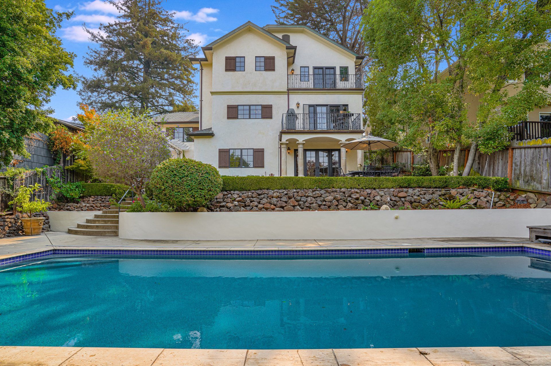 A large house with a pool, surrounded by trees. The house has multiple levels with balconies.