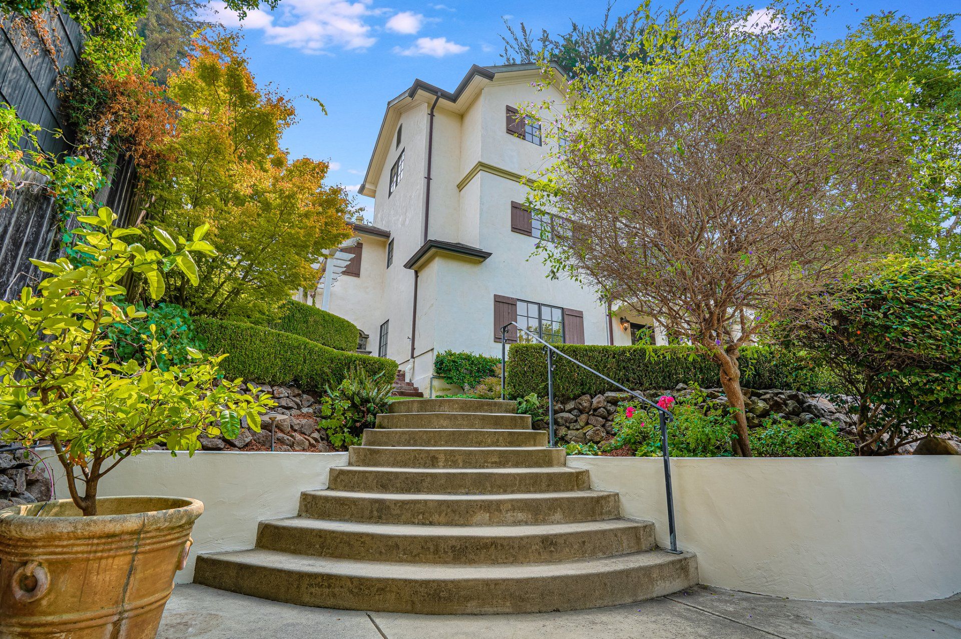 A white house with stairs leading up to it surrounded by trees and bushes.