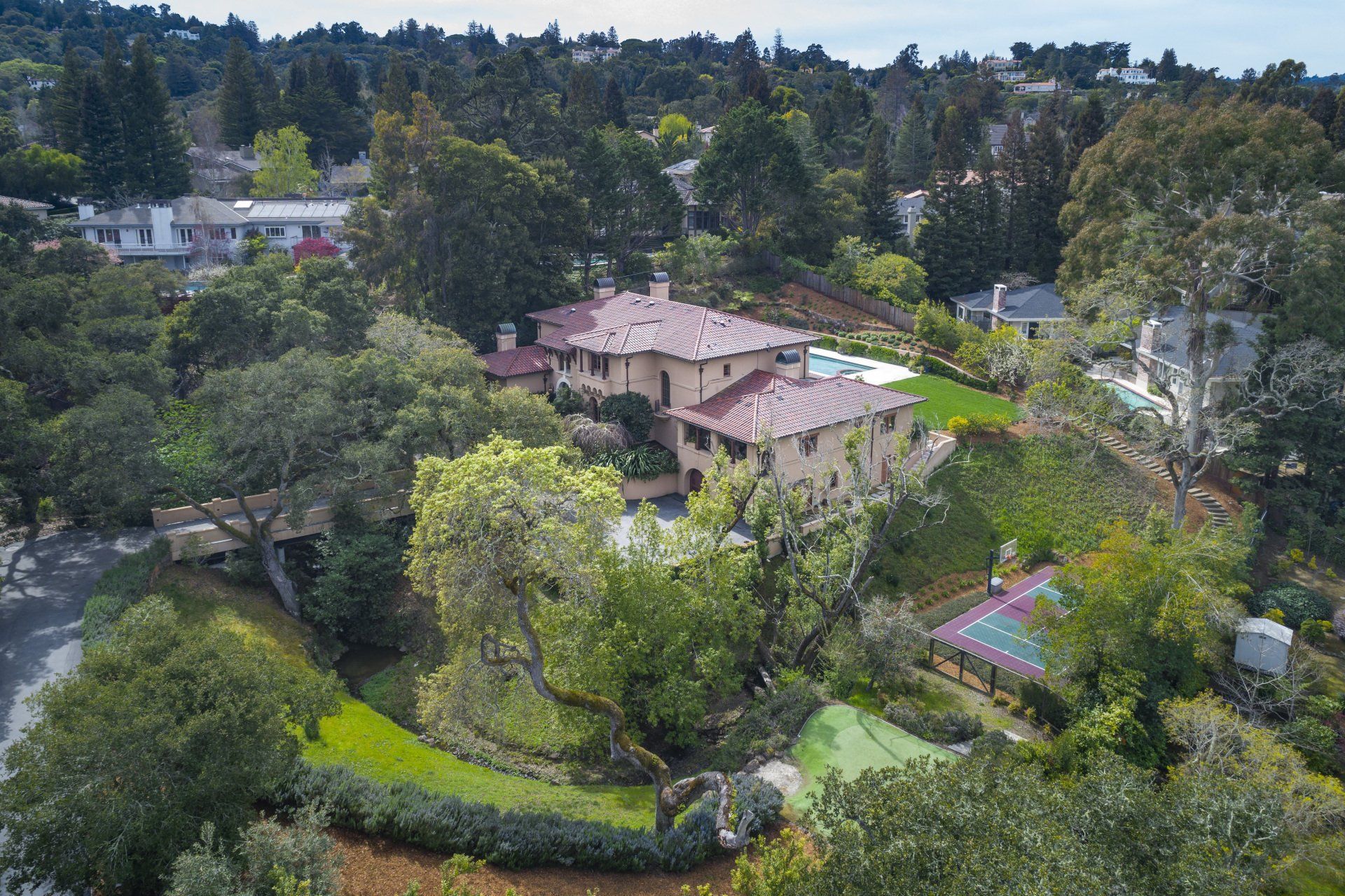 An aerial view of a large house surrounded by trees and a tennis court.