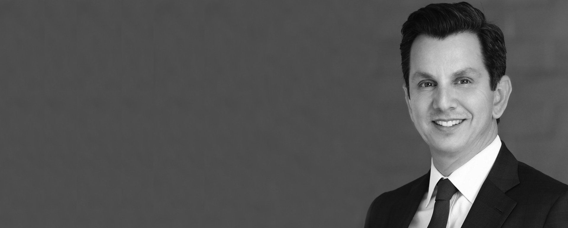 A man in a suit and tie is smiling in a black and white photo.