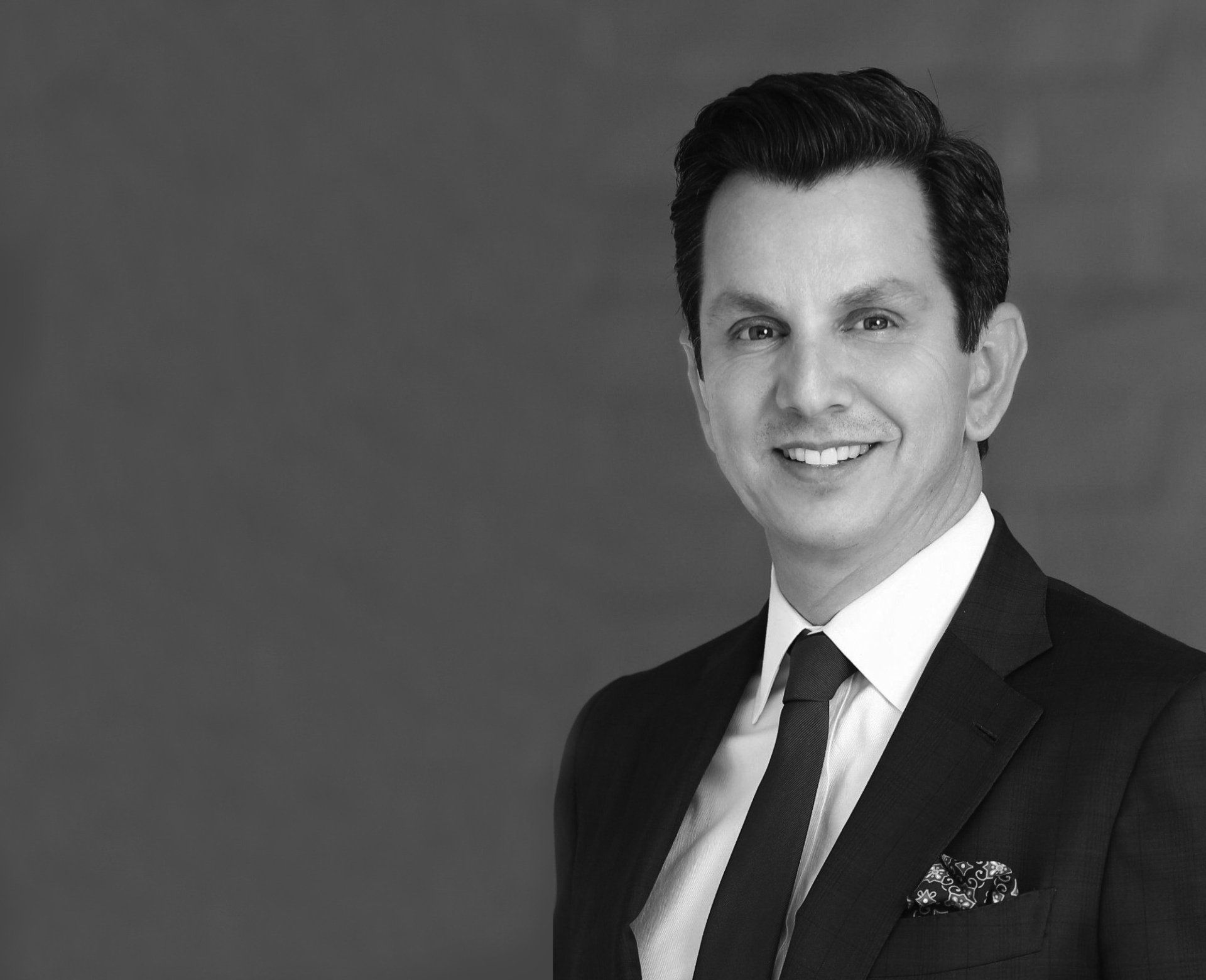 A man in a suit and tie is smiling in a black and white photo