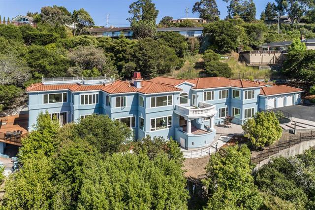 Large house with orange tile roof nestled in greenery on a hillside.