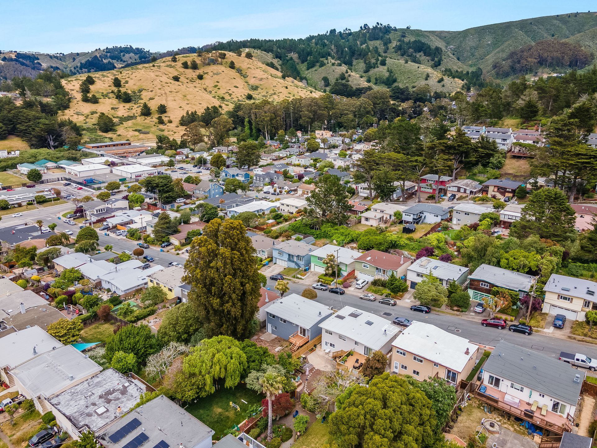 Aerial view of a neighborhood and green hills in the background on a sunny day.