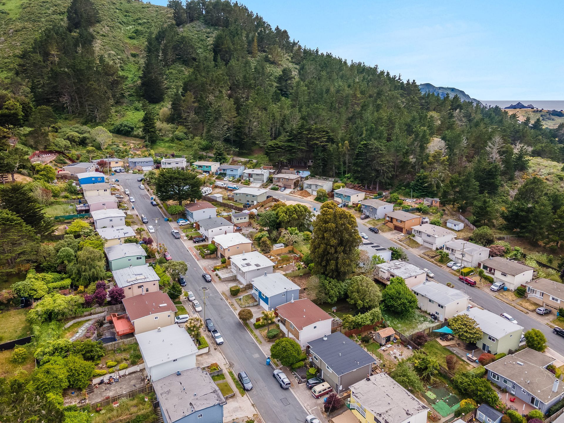 Aerial view of a residential neighborhood nestled on a hillside, surrounded by trees and a blue sky.