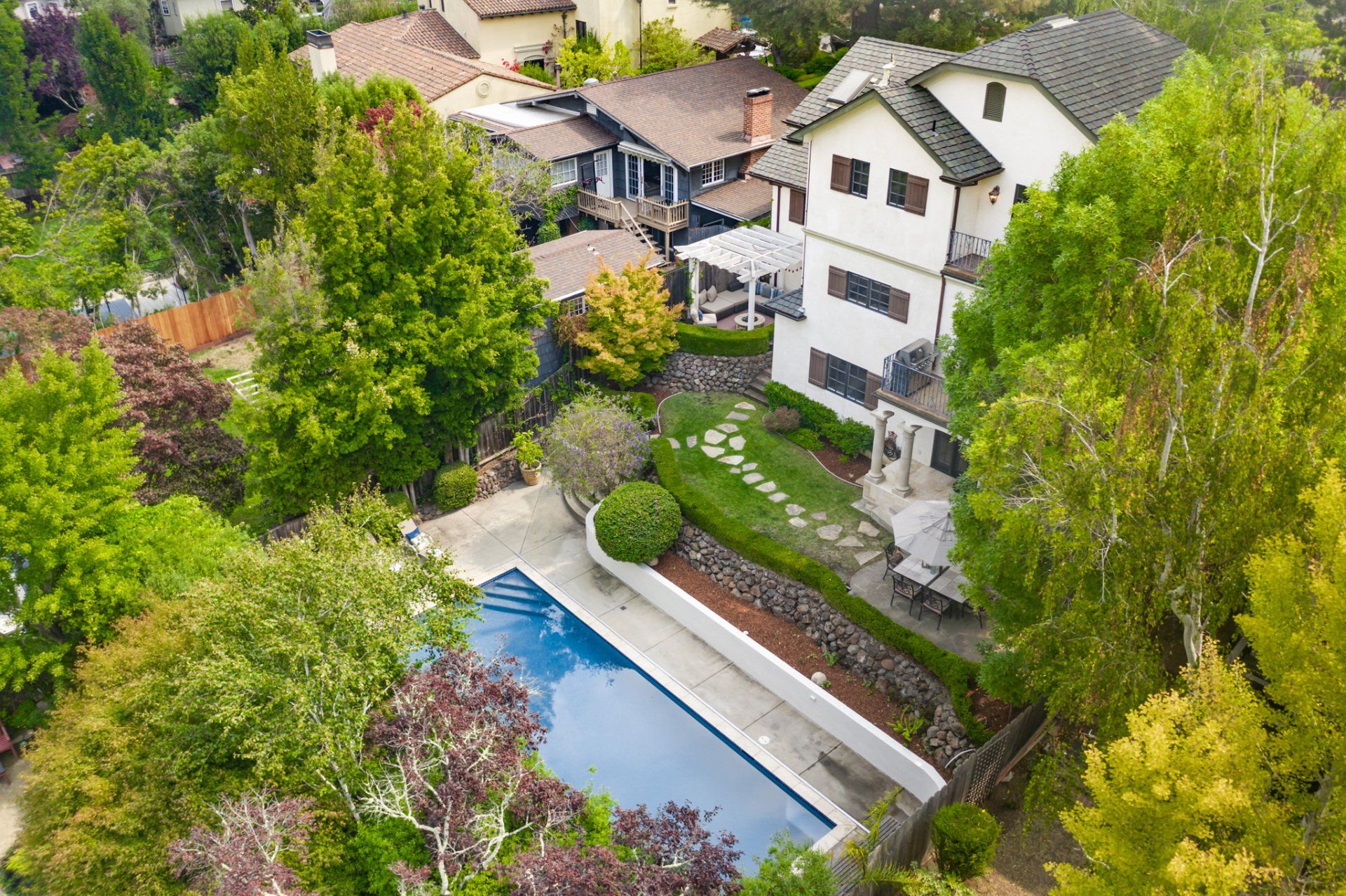 An aerial view of a house with a large swimming pool in the backyard surrounded by trees.