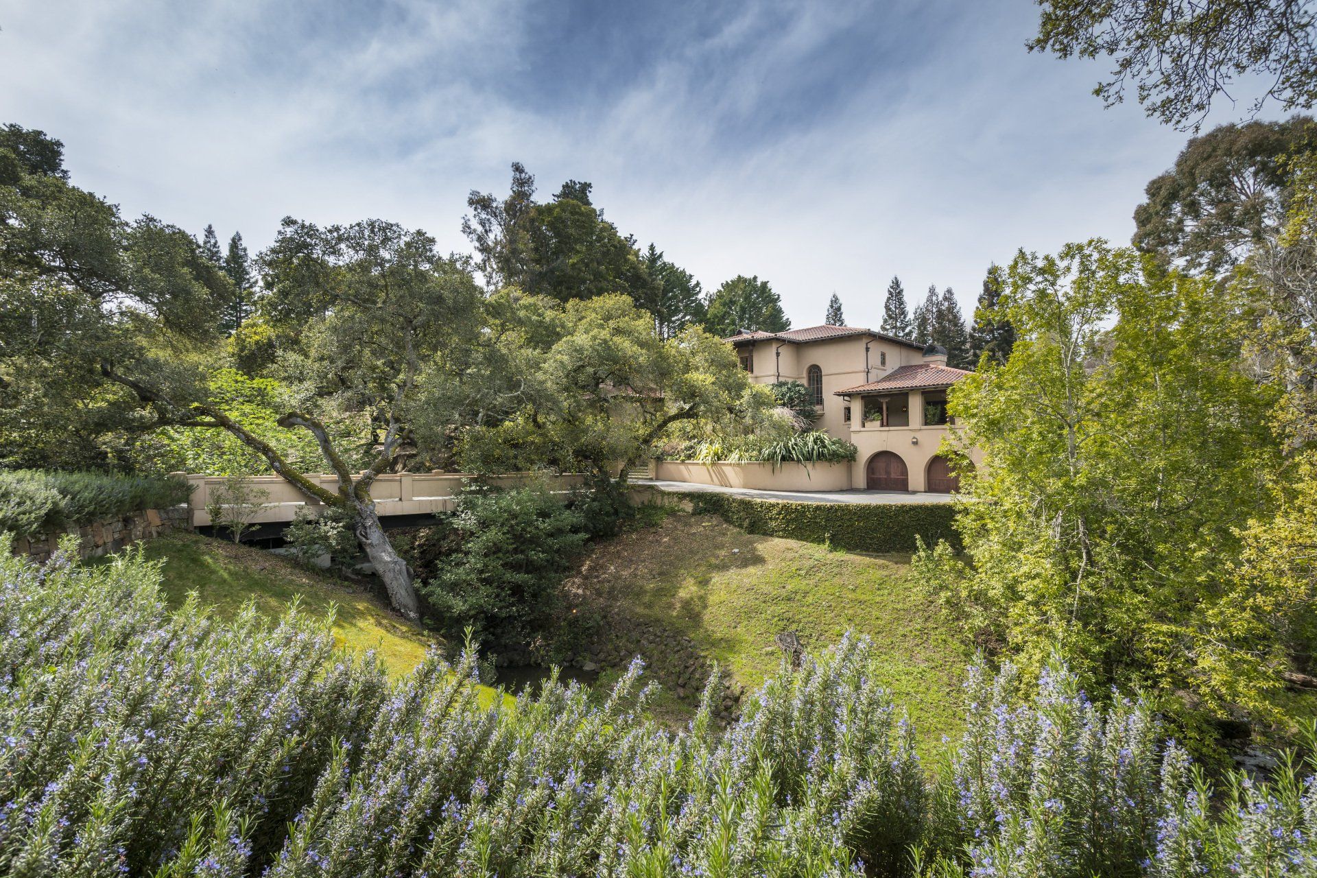 A large house is sitting on top of a hill surrounded by trees and bushes.