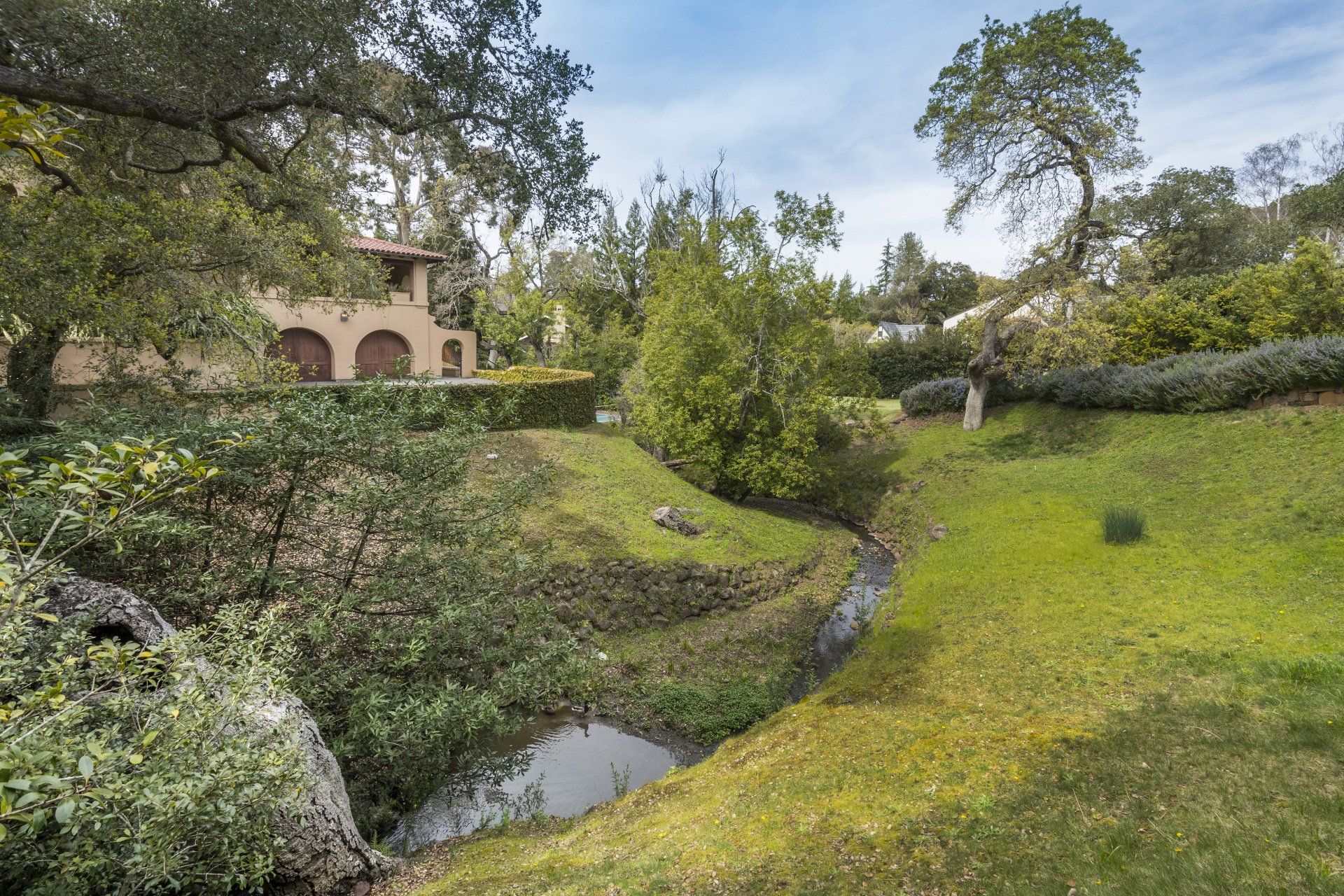 A house is sitting on top of a grassy hill next to a stream.