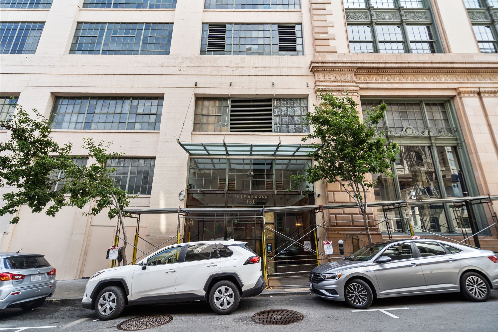 A building facade with parked cars. A white SUV and a silver sedan are visible.