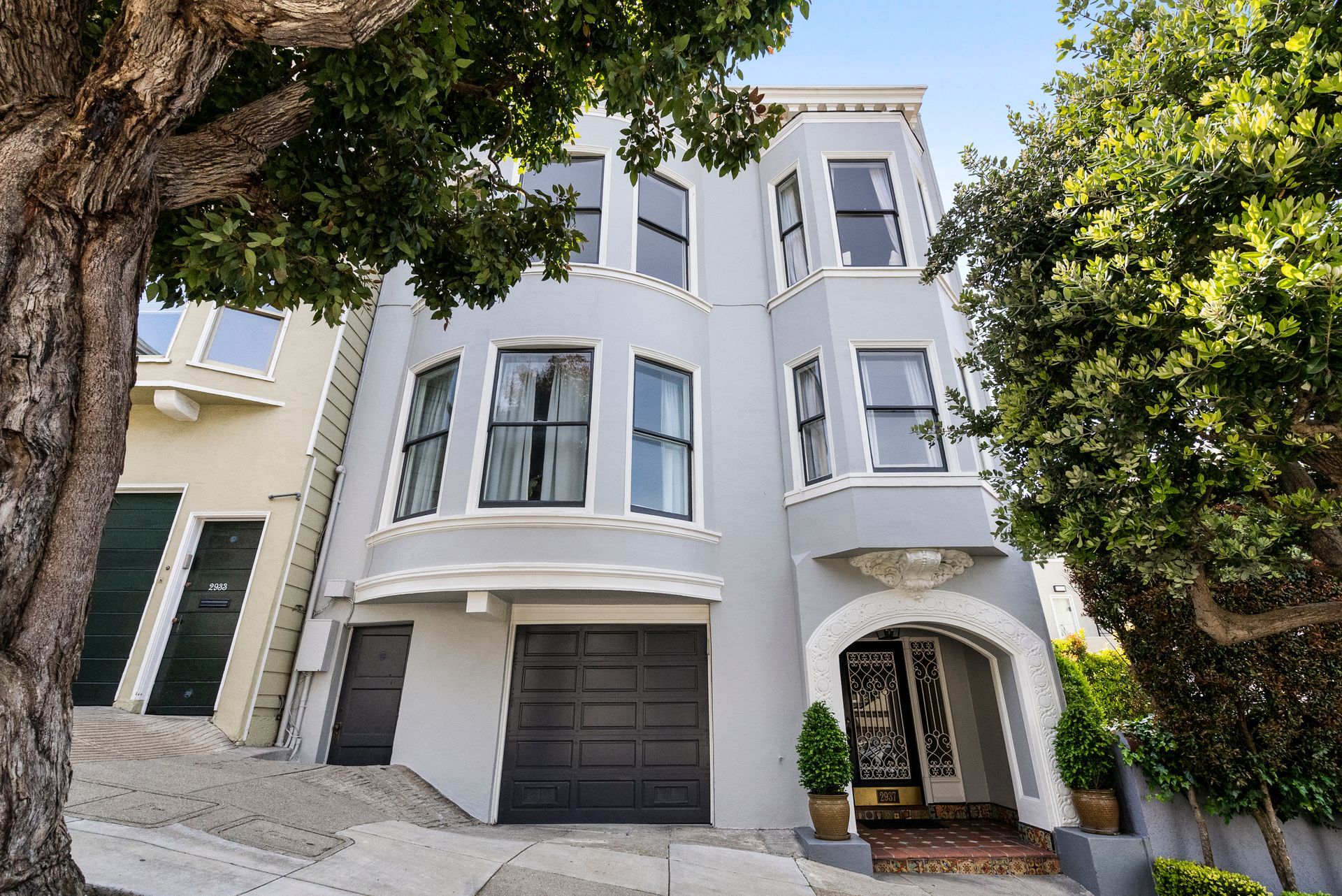 A large gray house with a black garage and a tree in front of it.