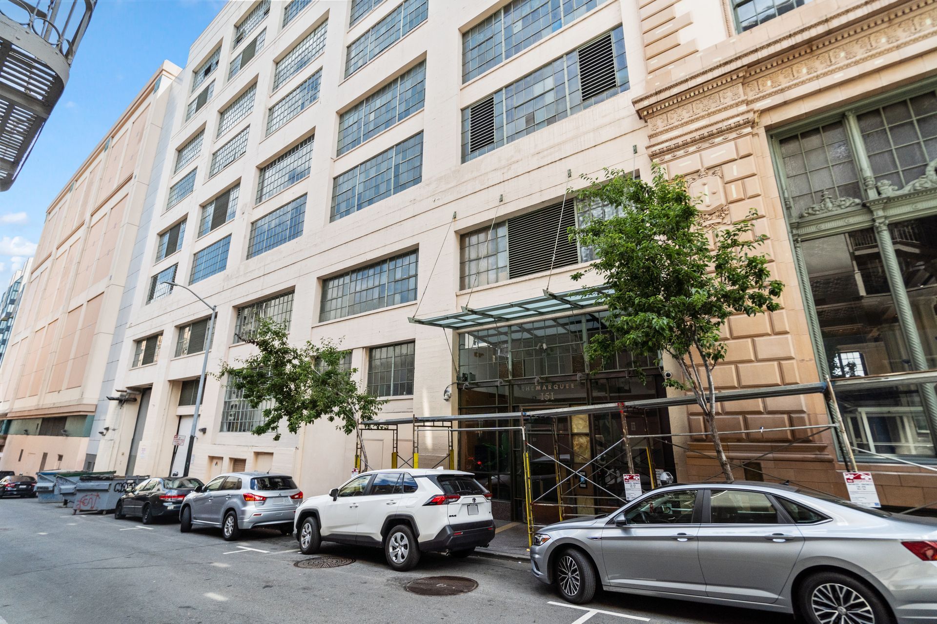 Street view of a multi-story building with parked cars in front.