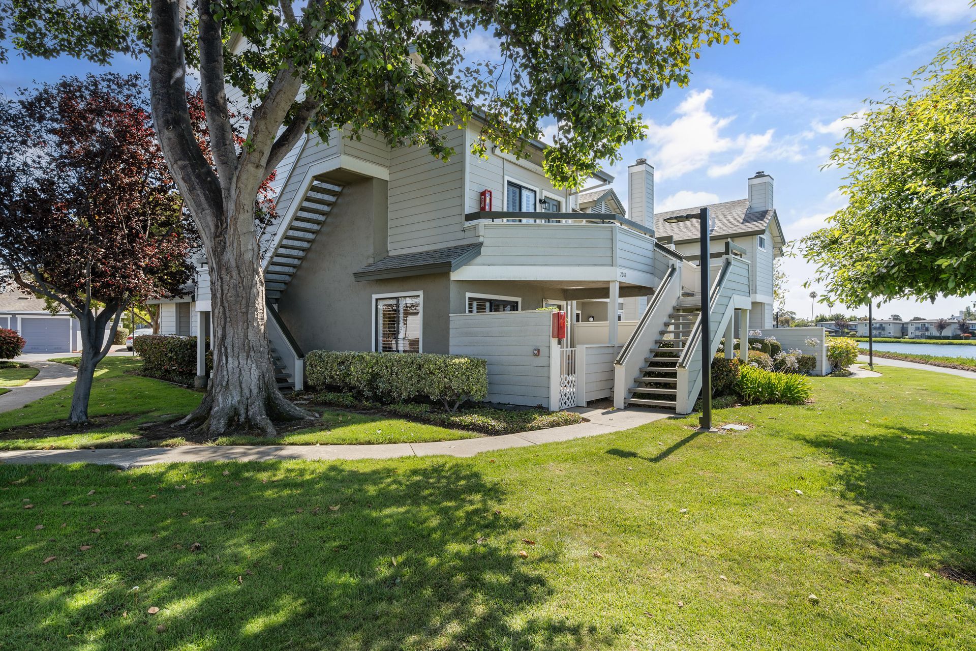 A house with stairs leading up to the second floor and a tree in front of it.