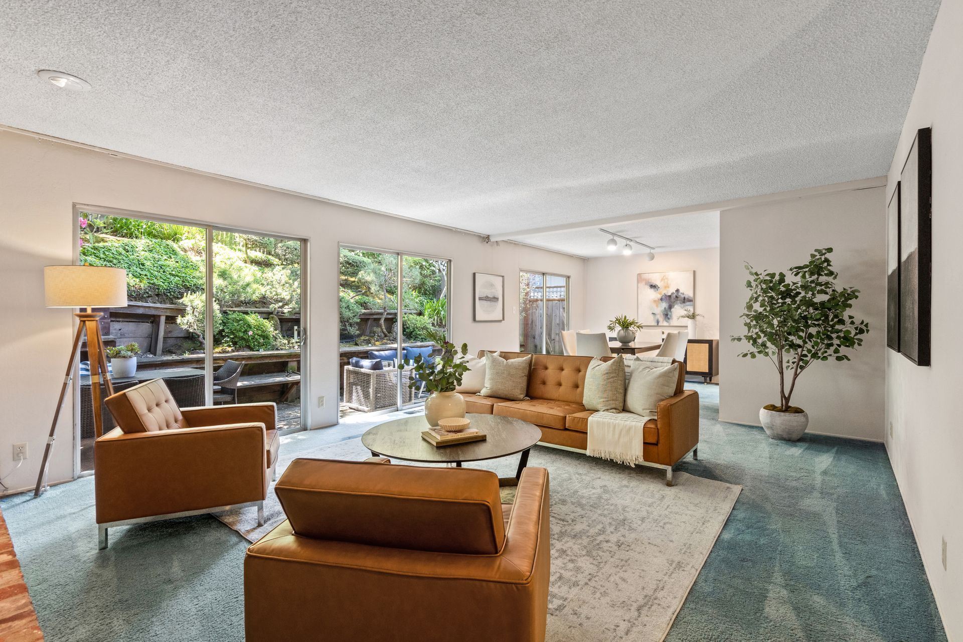 Living room with brown leather furniture, rug, round coffee table, and windows overlooking greenery. Turquoise carpet.