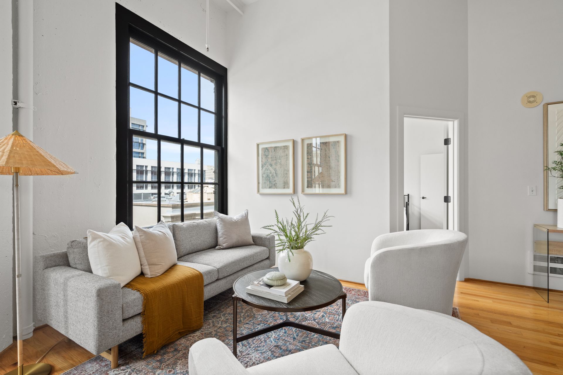 Living room with gray sofa, white chairs, and large window with black trim.