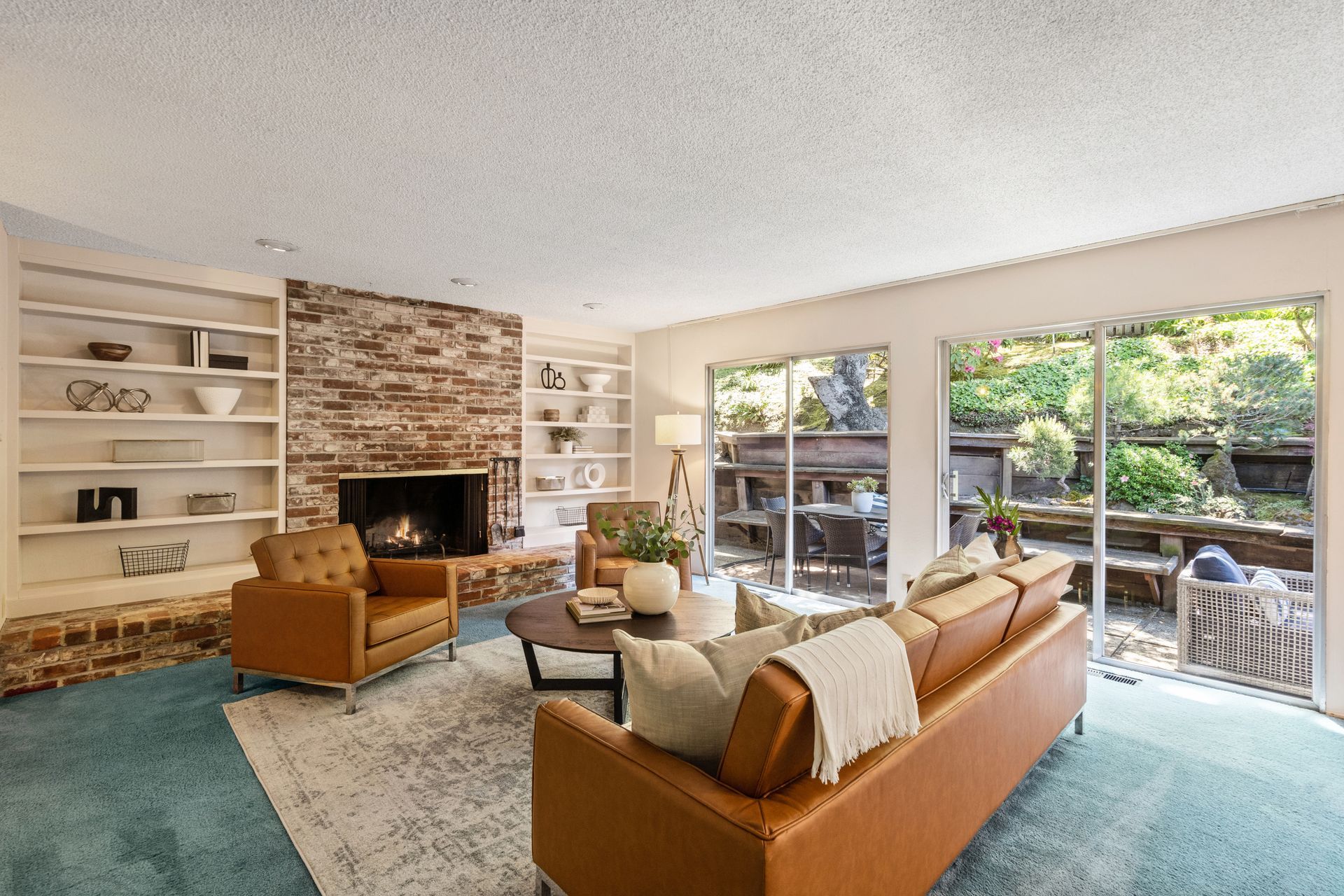 Living room with brick fireplace, built-in shelves, and sliding doors to a patio. Furnished with leather chairs and a sofa, plus a round coffee table.