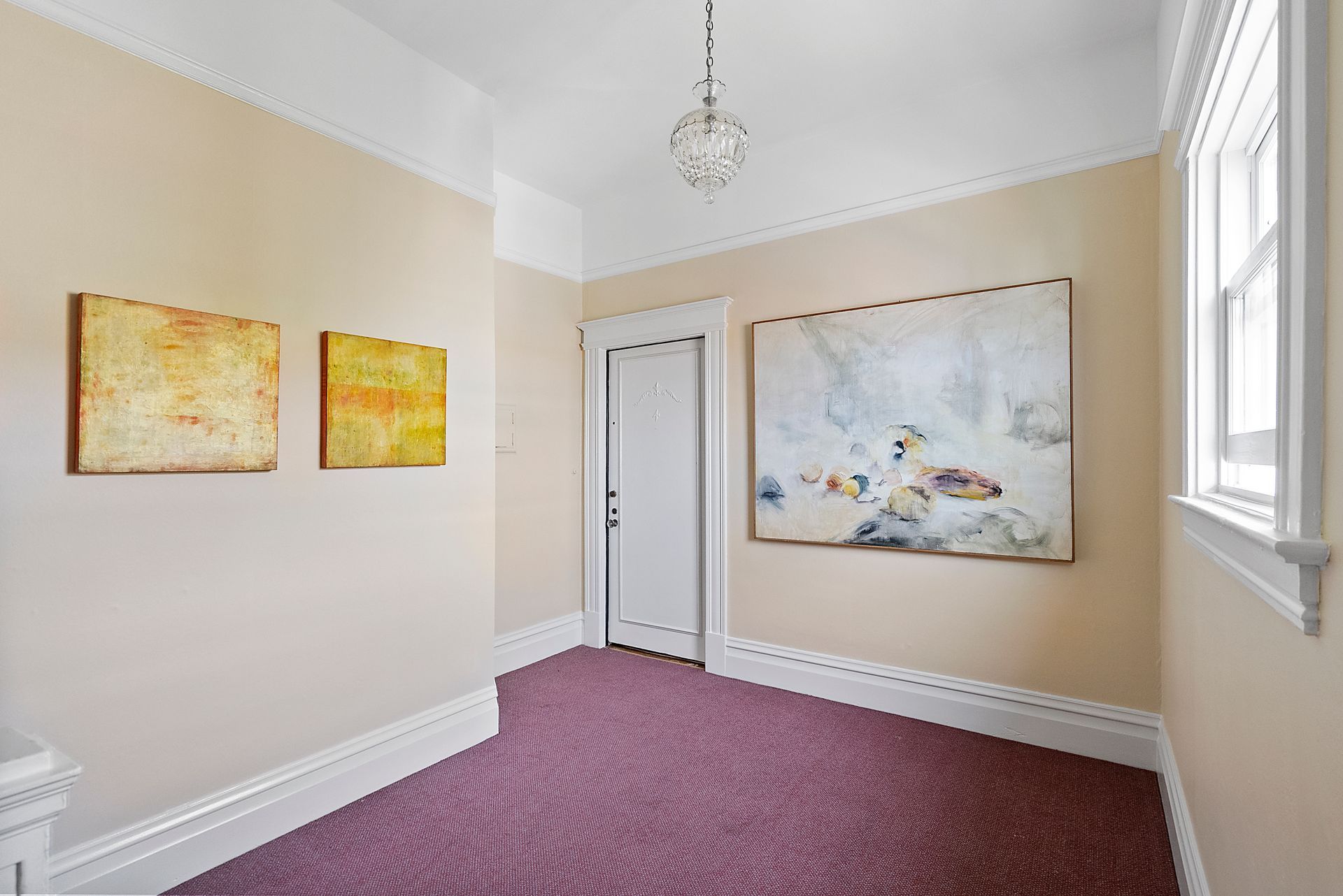 A hallway with two paintings on the wall and a purple carpet.