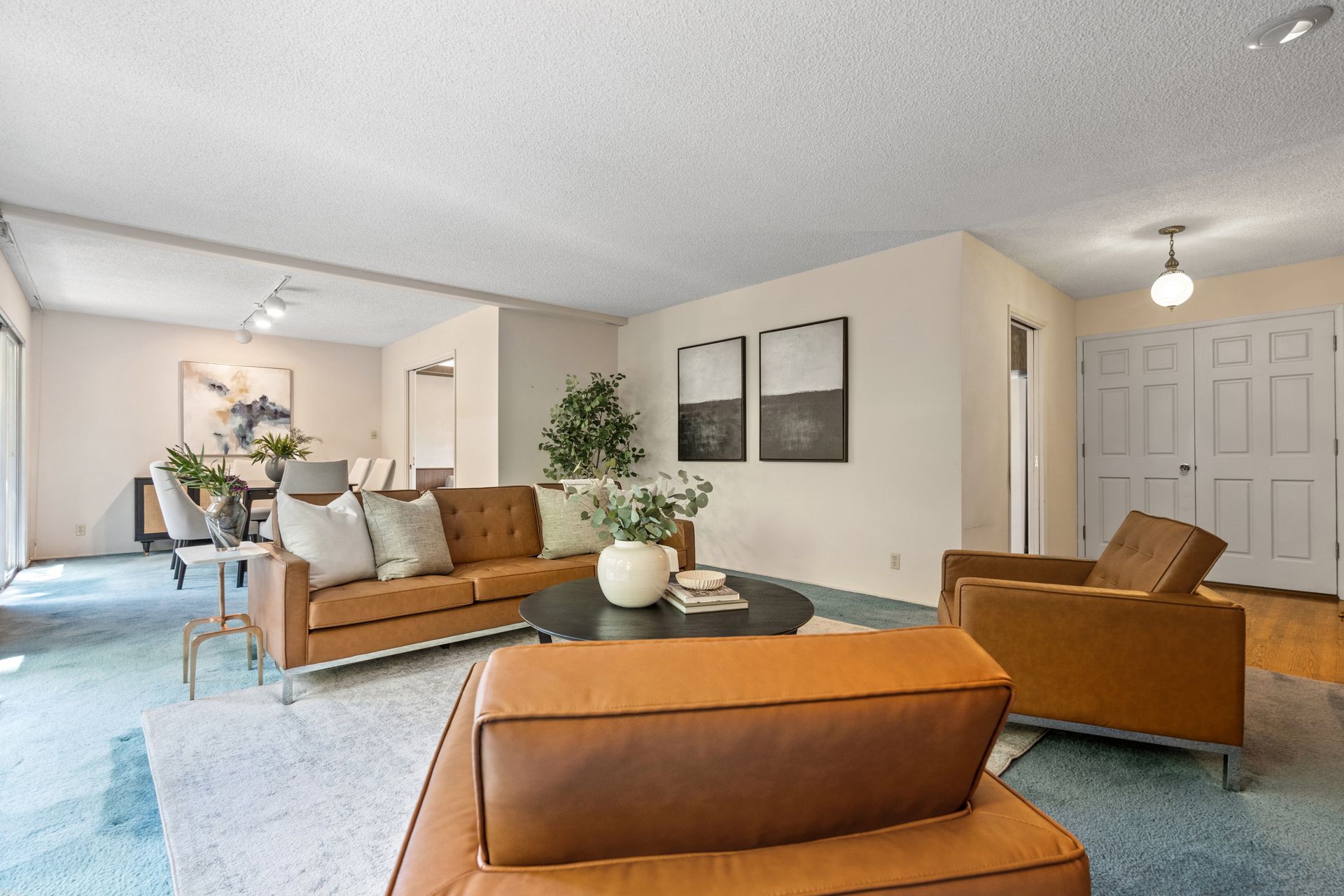 Spacious living room with brown leather furniture, a round coffee table, and a view into the dining area.