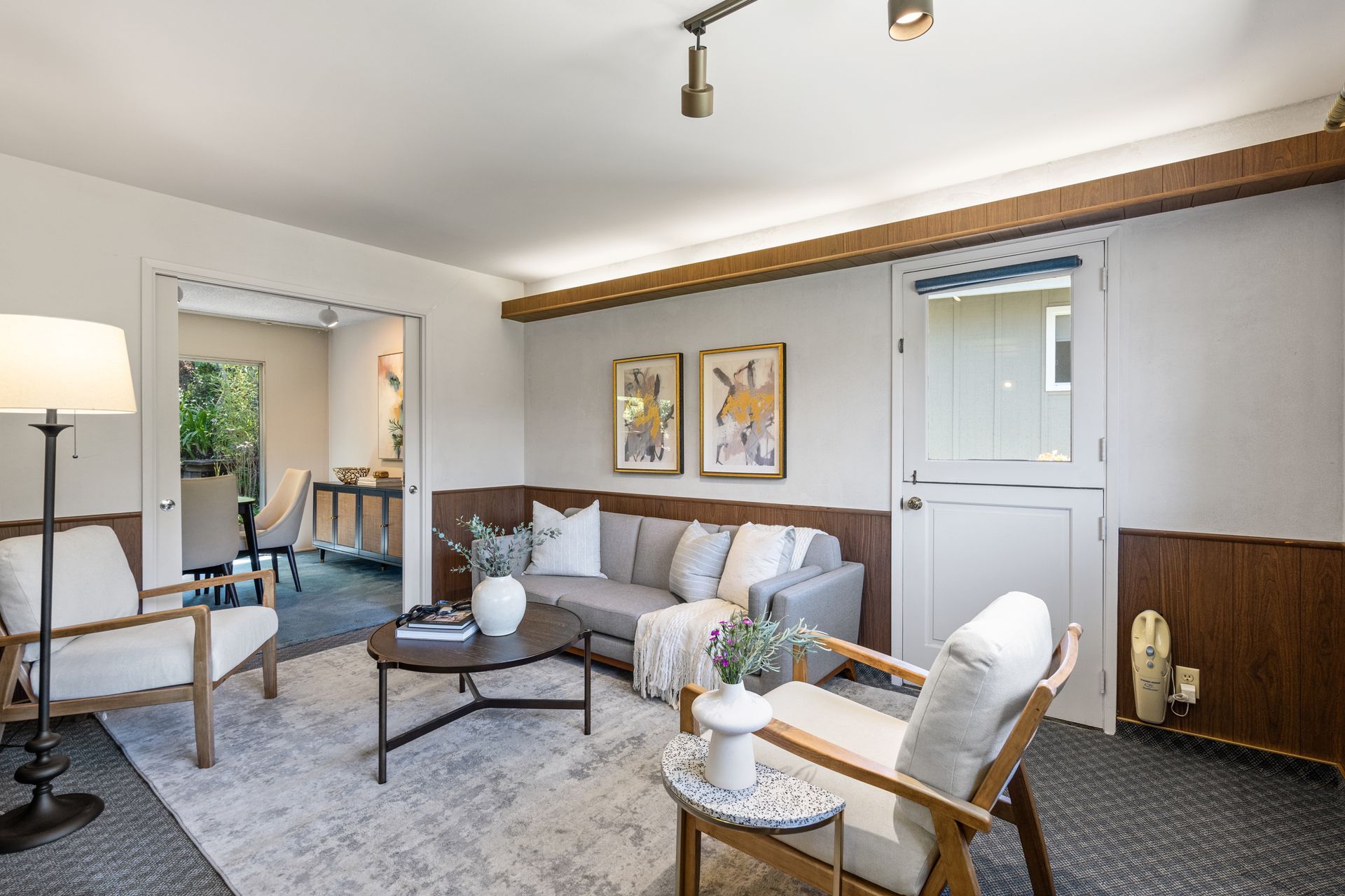 A room with light gray sofa, two armchairs, a coffee table, and a rug. The walls are painted white and paneled with wood.