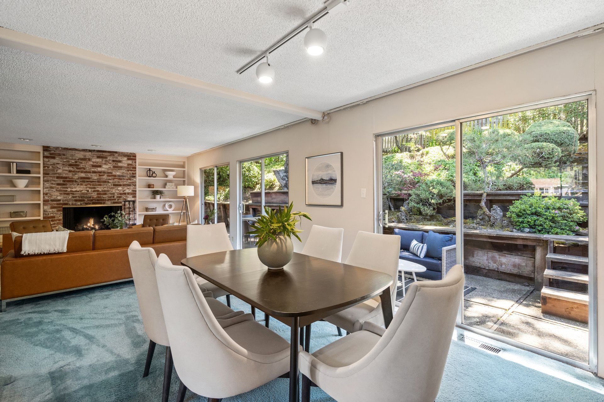 Dining room with a dark wood table and white chairs, open to a patio with lush greenery.