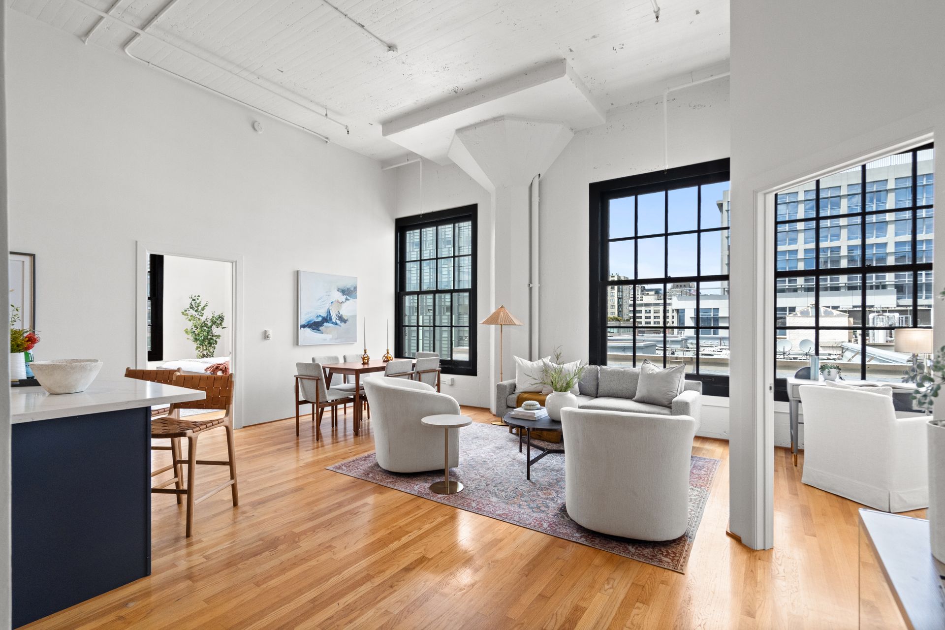 Bright, open room with hardwood floors, off-white walls, large windows, and modern furniture.