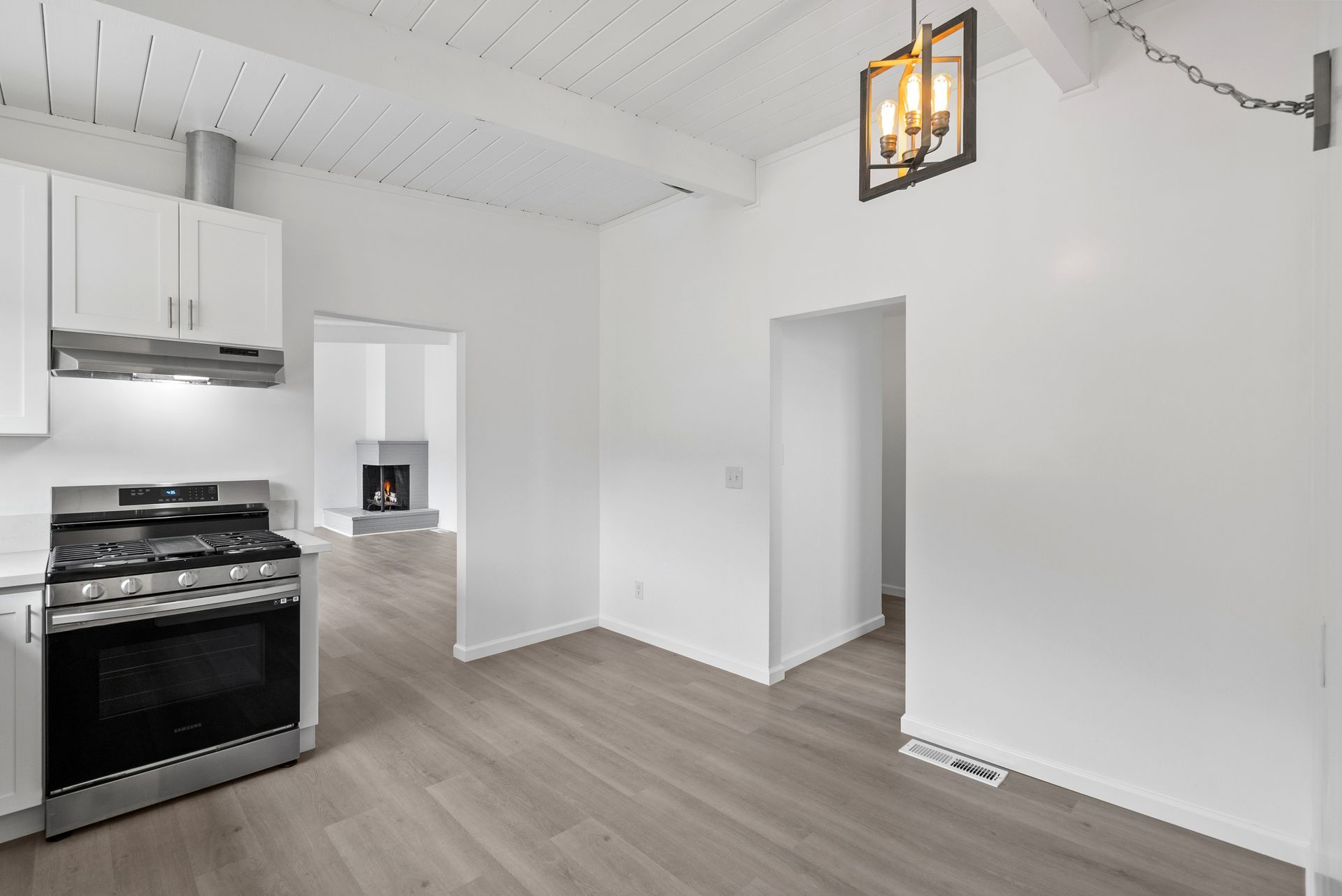 An empty kitchen with white cabinets , a stove , and a light.