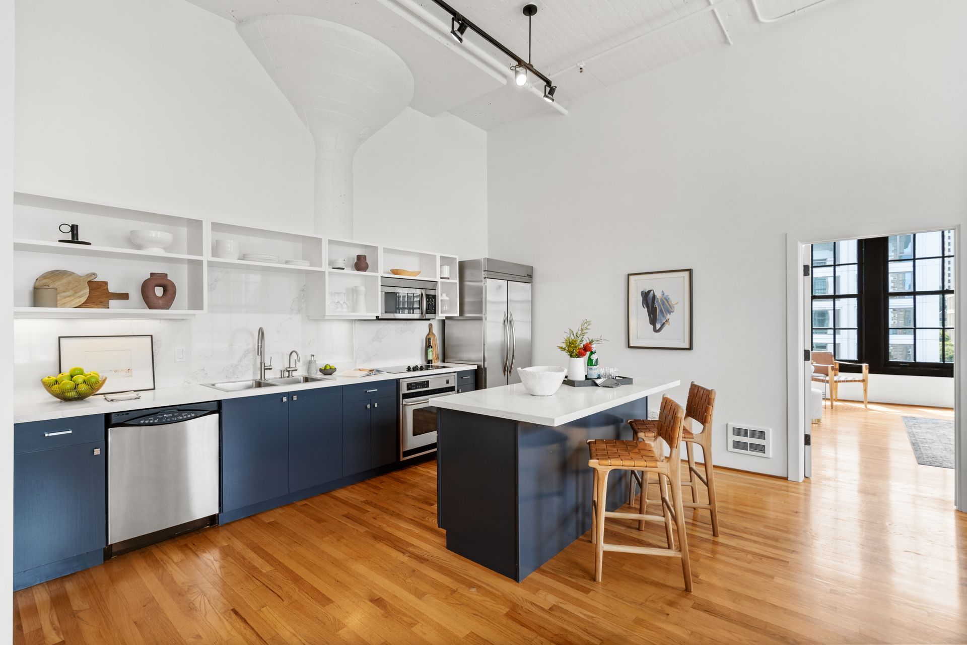 Modern kitchen with gun-metal blue-grey cabinets, white counters, stainless steel appliances, island with stools, and hardwood floors.