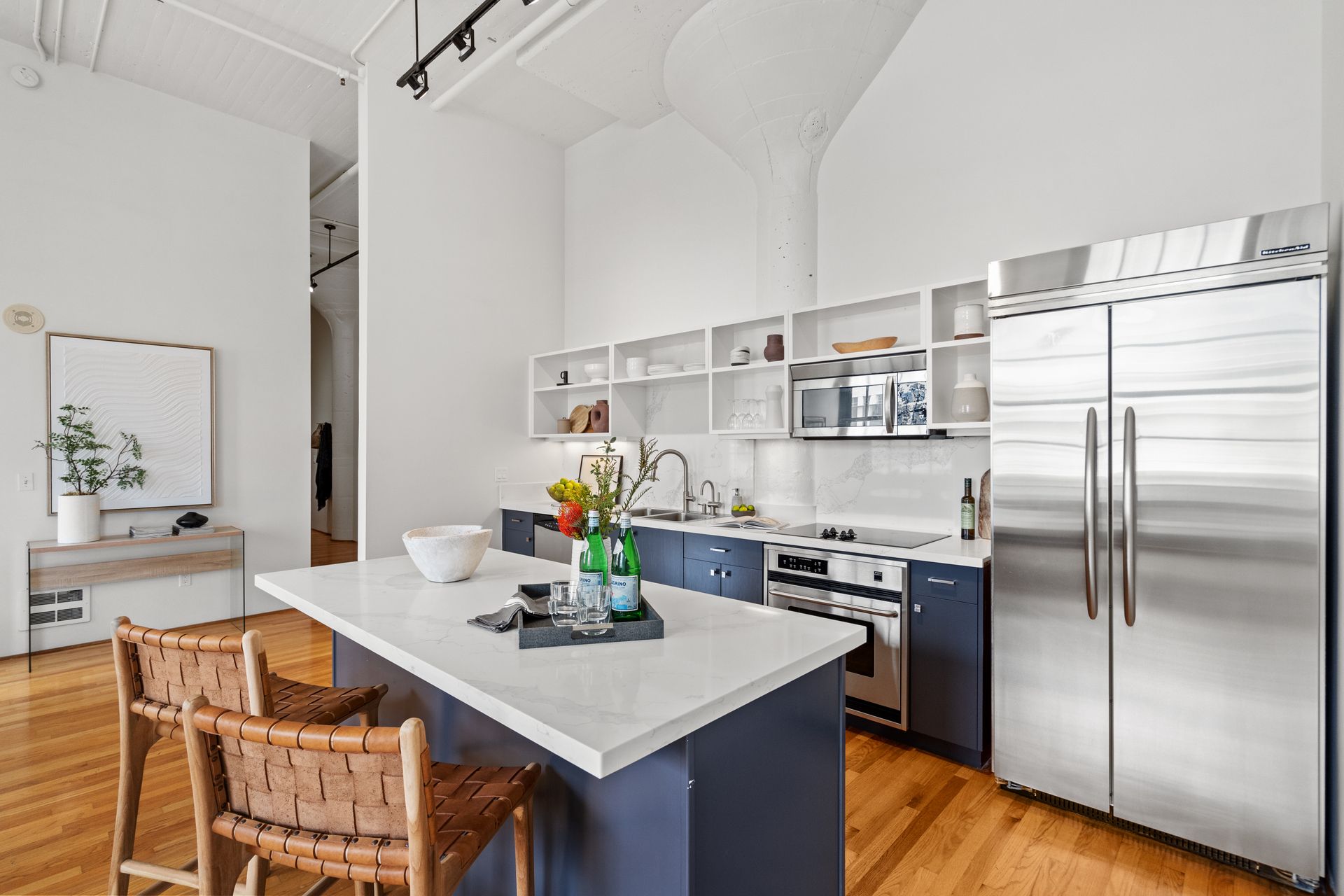 Modern kitchen with an island, stainless steel appliances, white countertops and open shelving, wood floors.