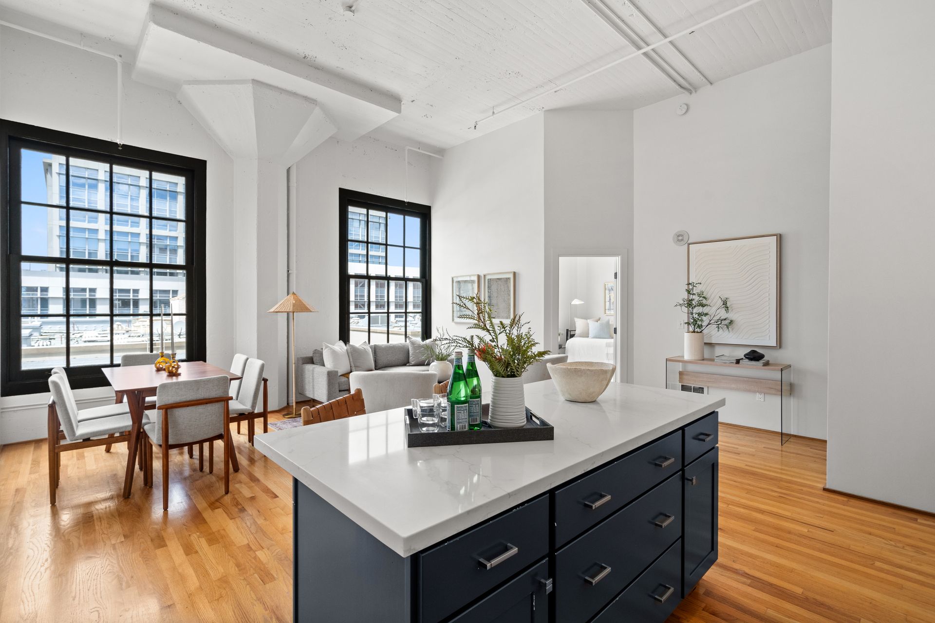 Open-concept loft with kitchen island, dining table, living room, large windows, and hardwood floors.