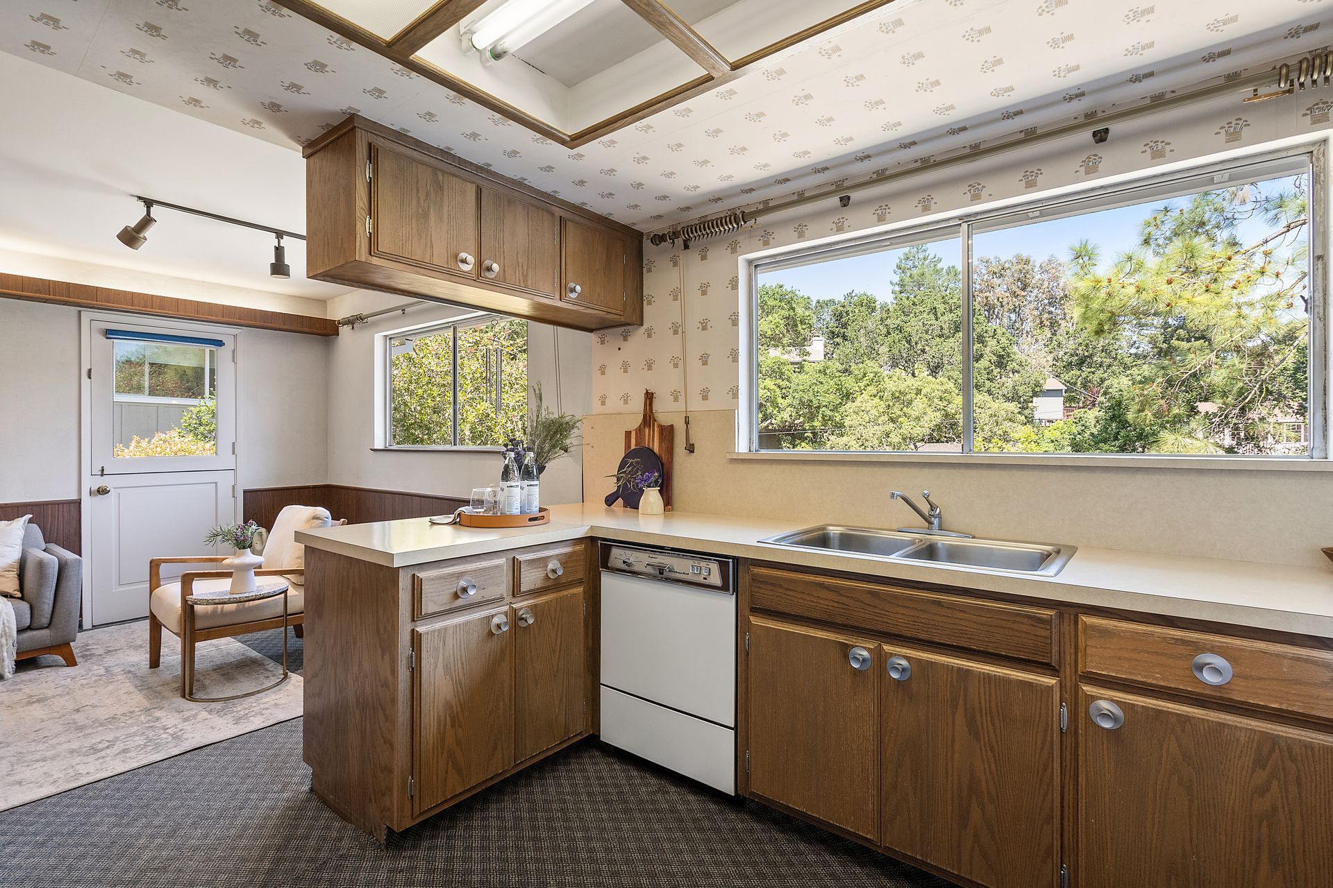 Kitchen with wood cabinets, white appliances, a sink, and a window overlooking trees.