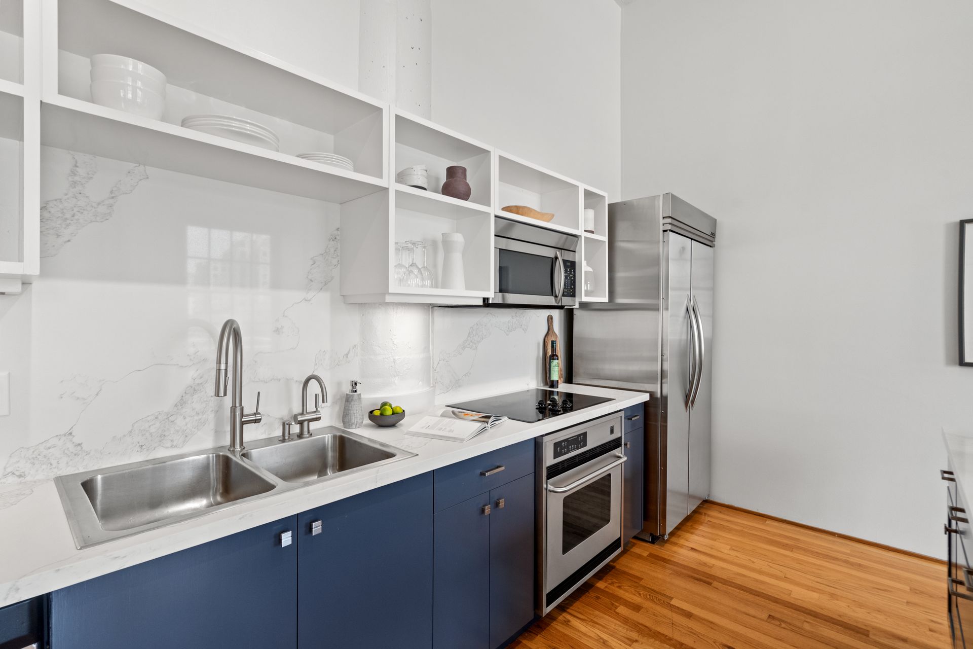 Modern kitchen with gun-metal blue-grey cabinets, stainless steel appliances, and white marble backsplash.