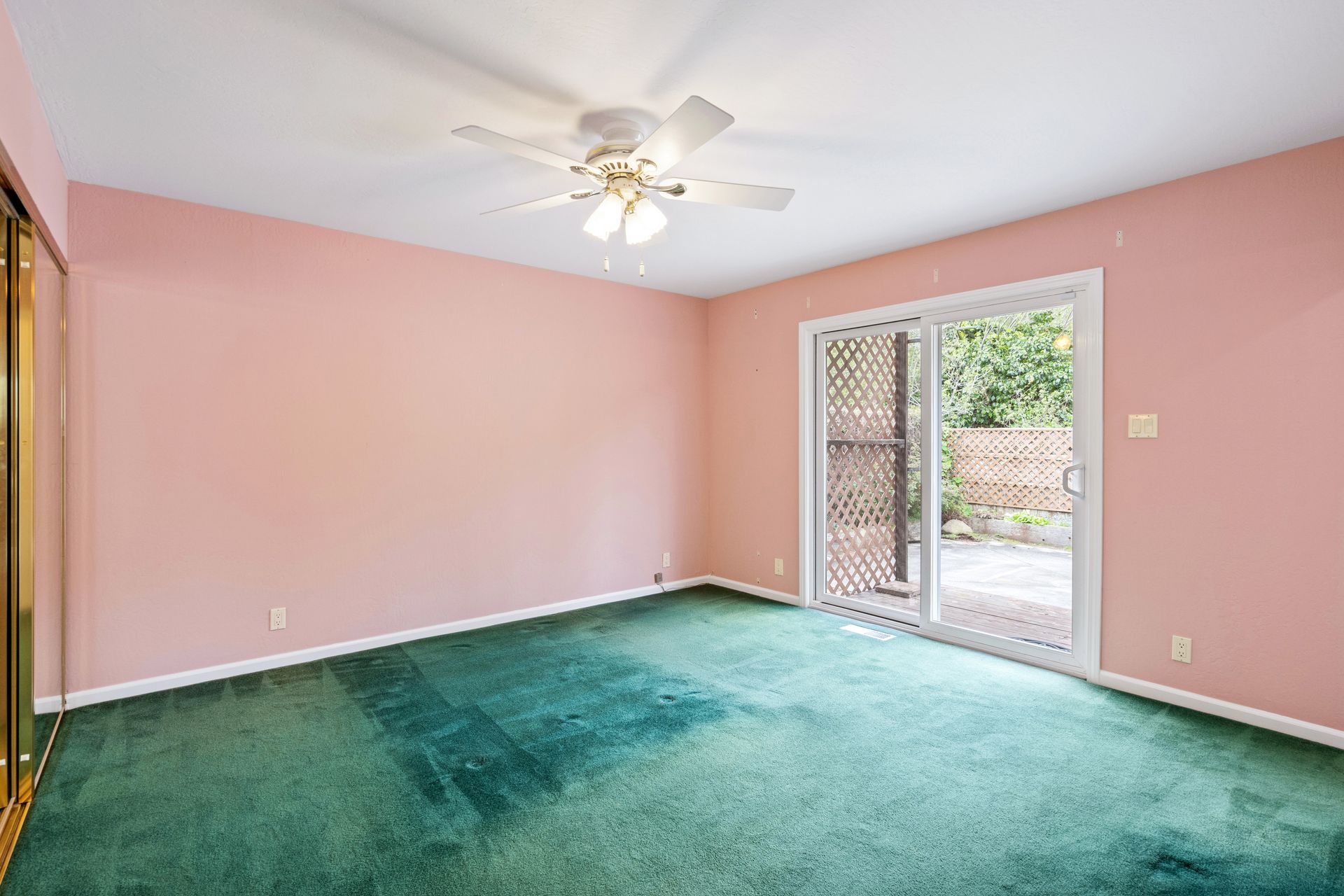 An empty room with pink walls and green carpet and a ceiling fan.