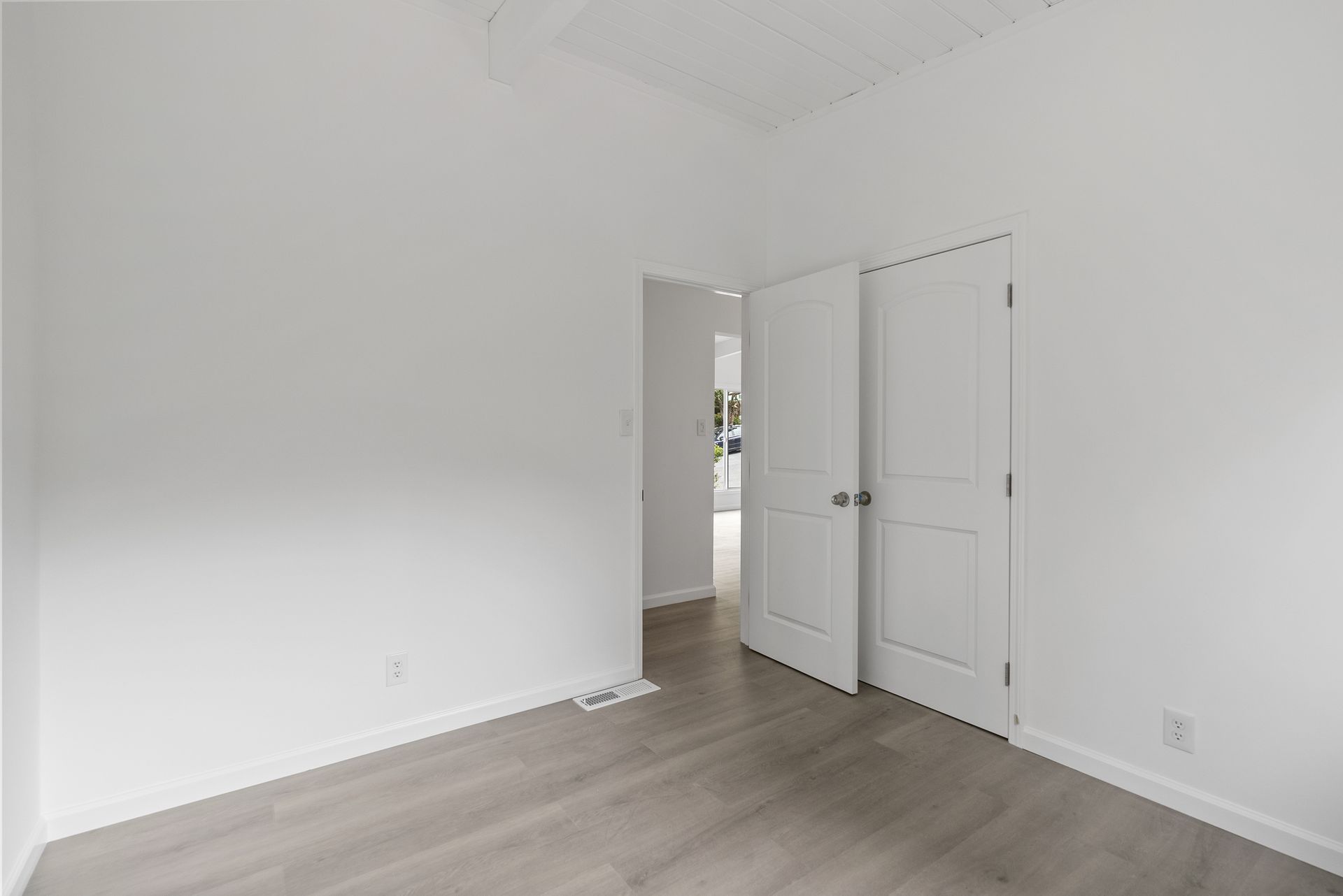 An empty bedroom with hardwood floors and white walls.