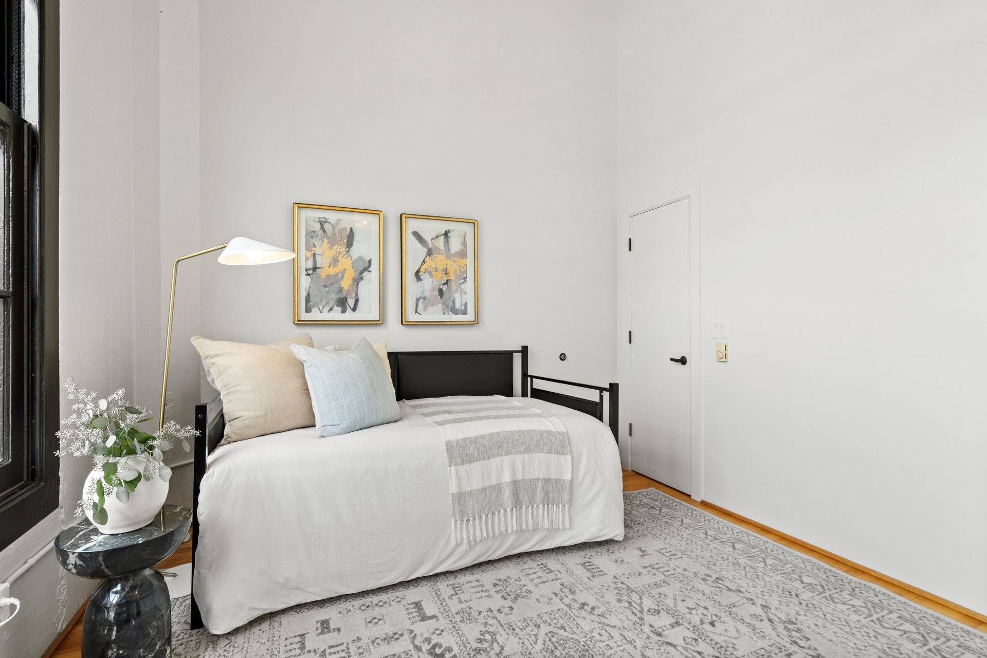 Bedroom with daybed, gold art, floor lamp, black side table, rug, and off-white walls.