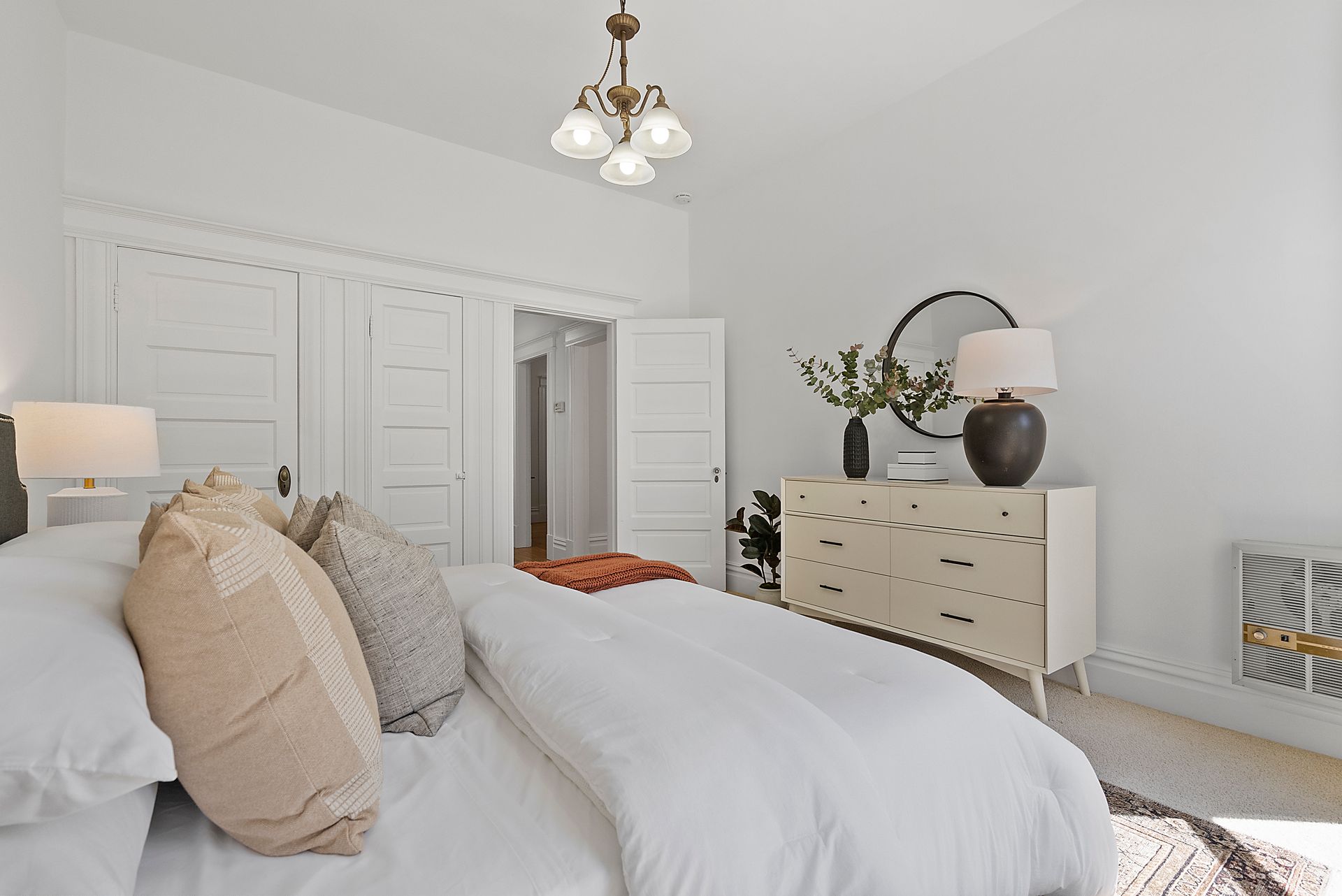 A bedroom with a bed , dresser , lamp and mirror.