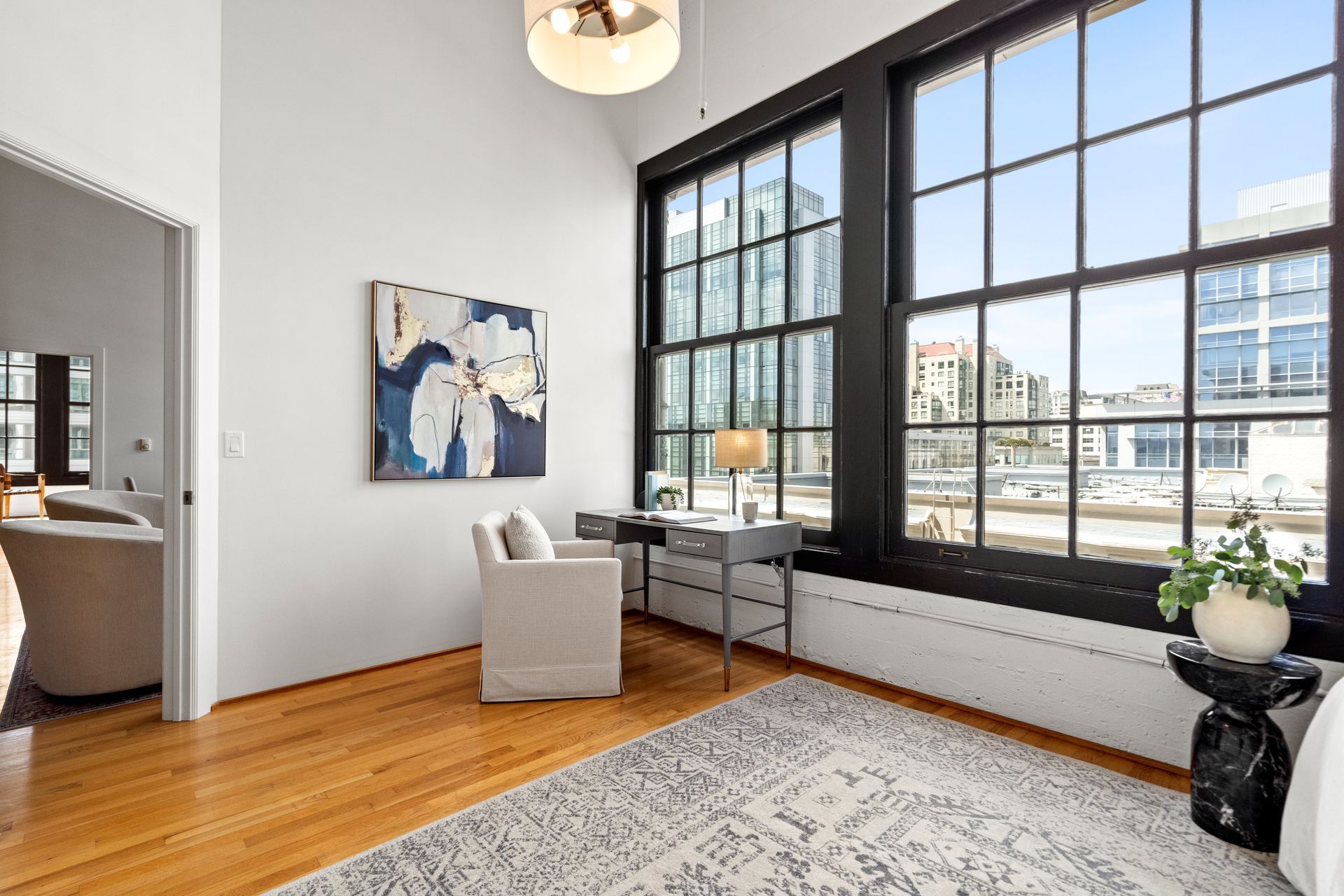 Bright room with large black-framed windows, a desk, chair, and abstract art on the wall.