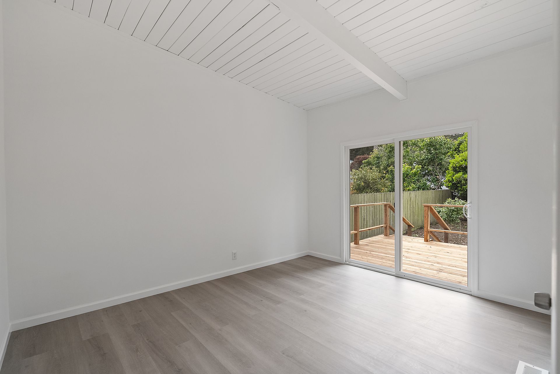 An empty room with hardwood floors and sliding glass doors leading to a deck.