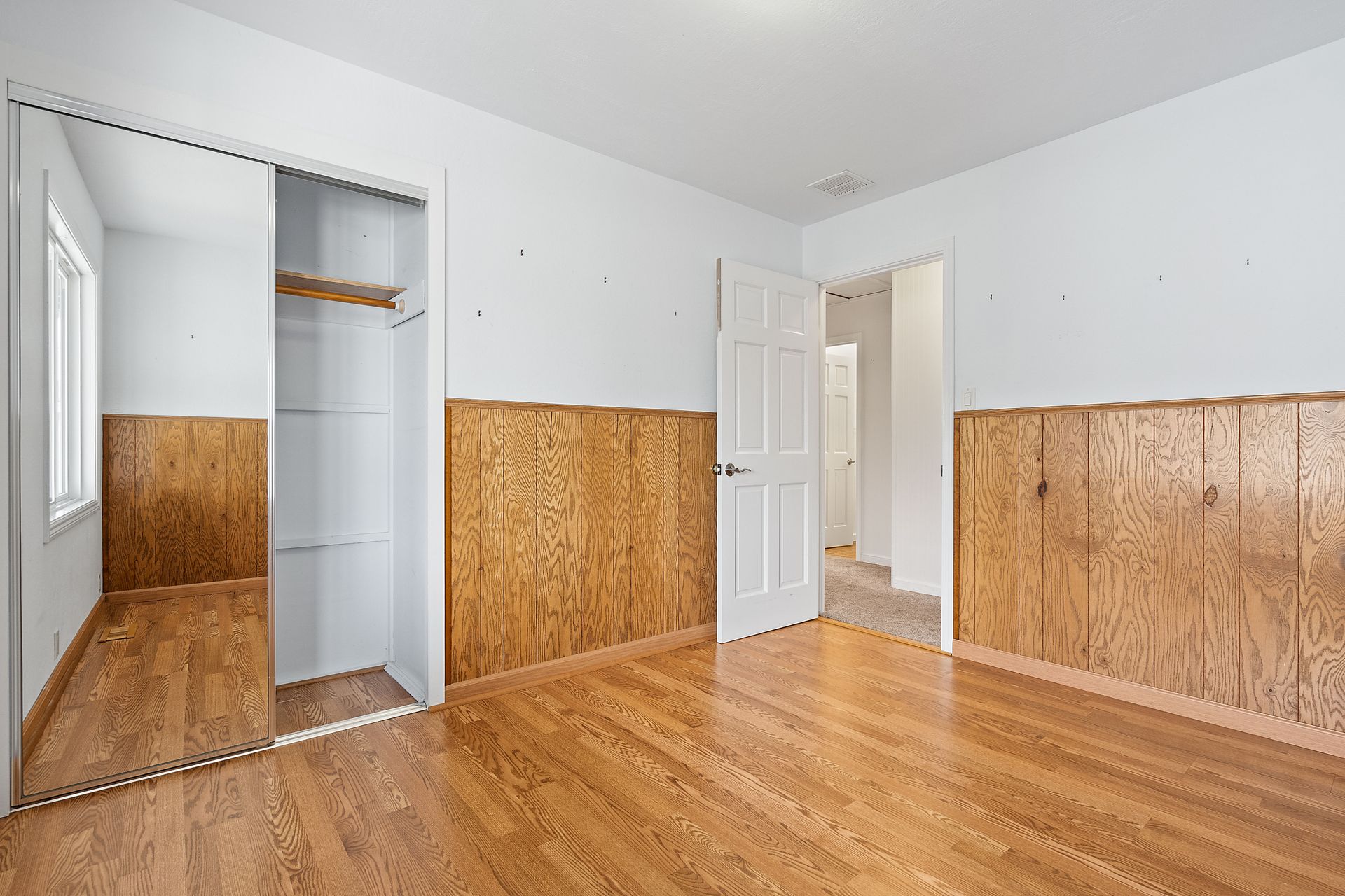 An empty bedroom with hardwood floors and white walls.