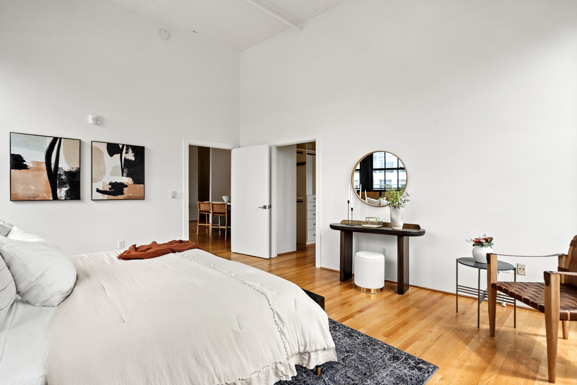 Spacious off-white bedroom with hardwood floors. A bed, vanity, and artwork are in the room.