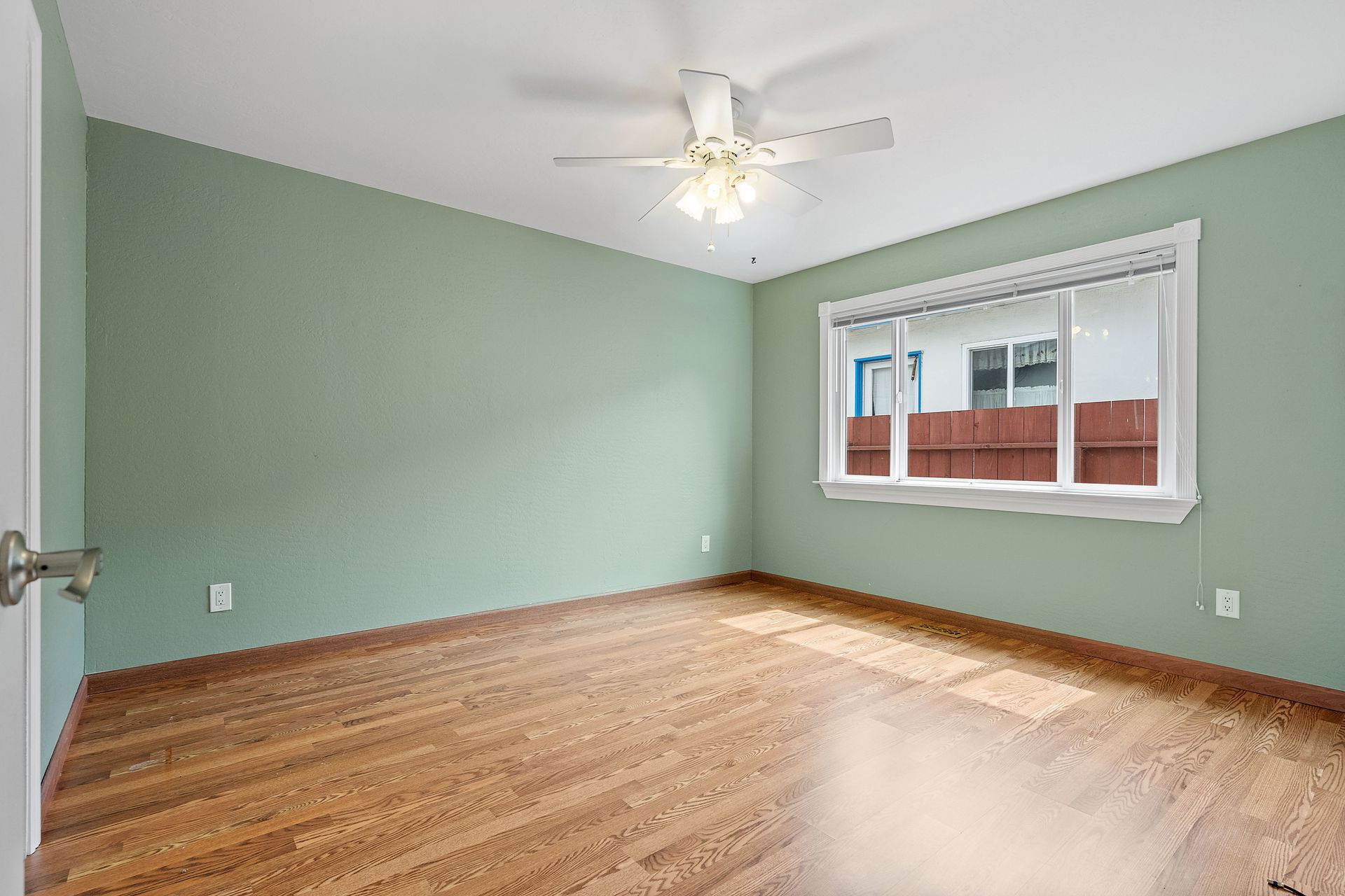 An empty bedroom with green walls and hardwood floors and a ceiling fan.