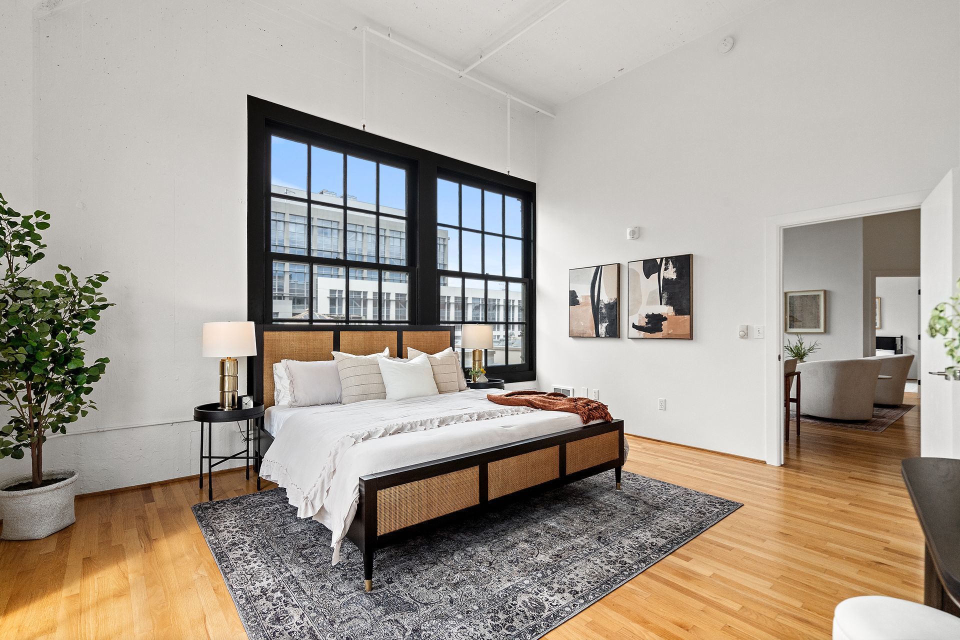 Spacious bedroom with large windows, wood floors, a bed with a woven headboard, and a rug.