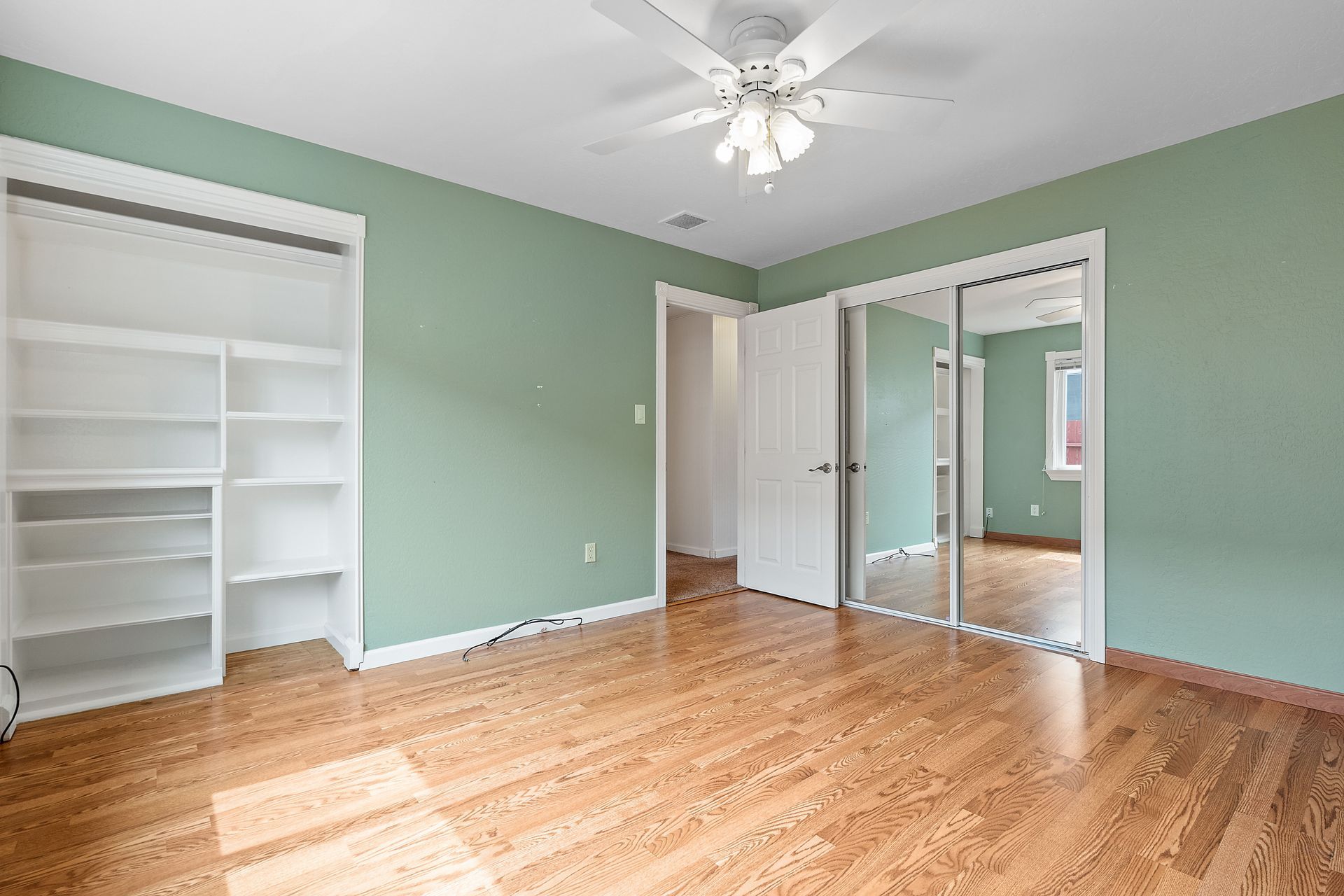 An empty bedroom with green walls and hardwood floors and a ceiling fan.