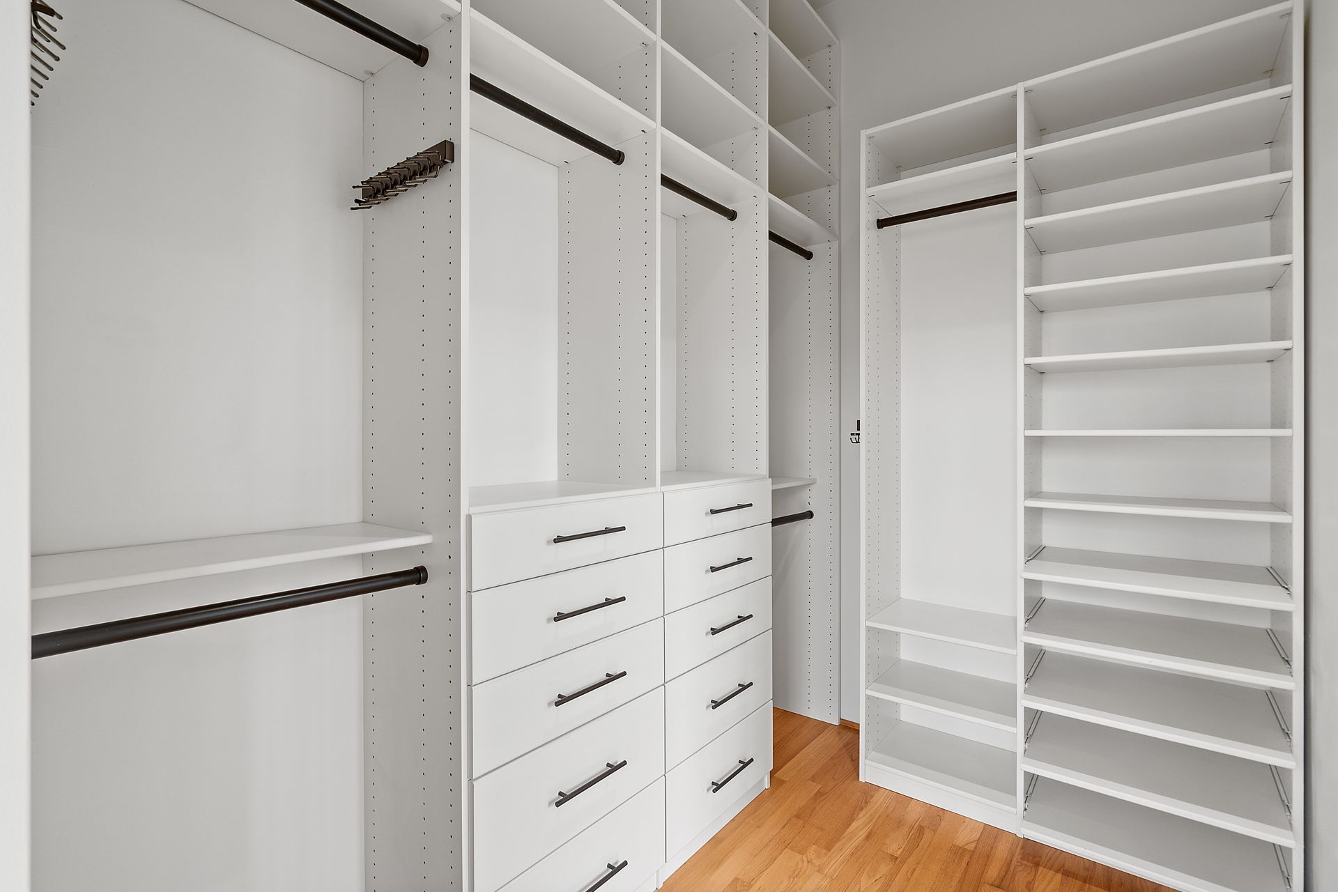 White custom closet with drawers, shelves, and hanging rods; wooden floor.
