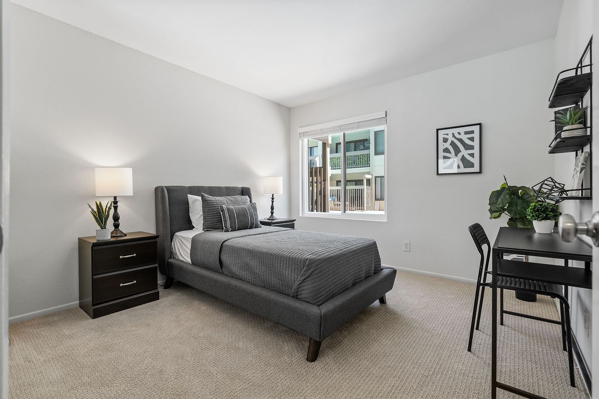A bedroom with a bed , nightstand , desk and window.