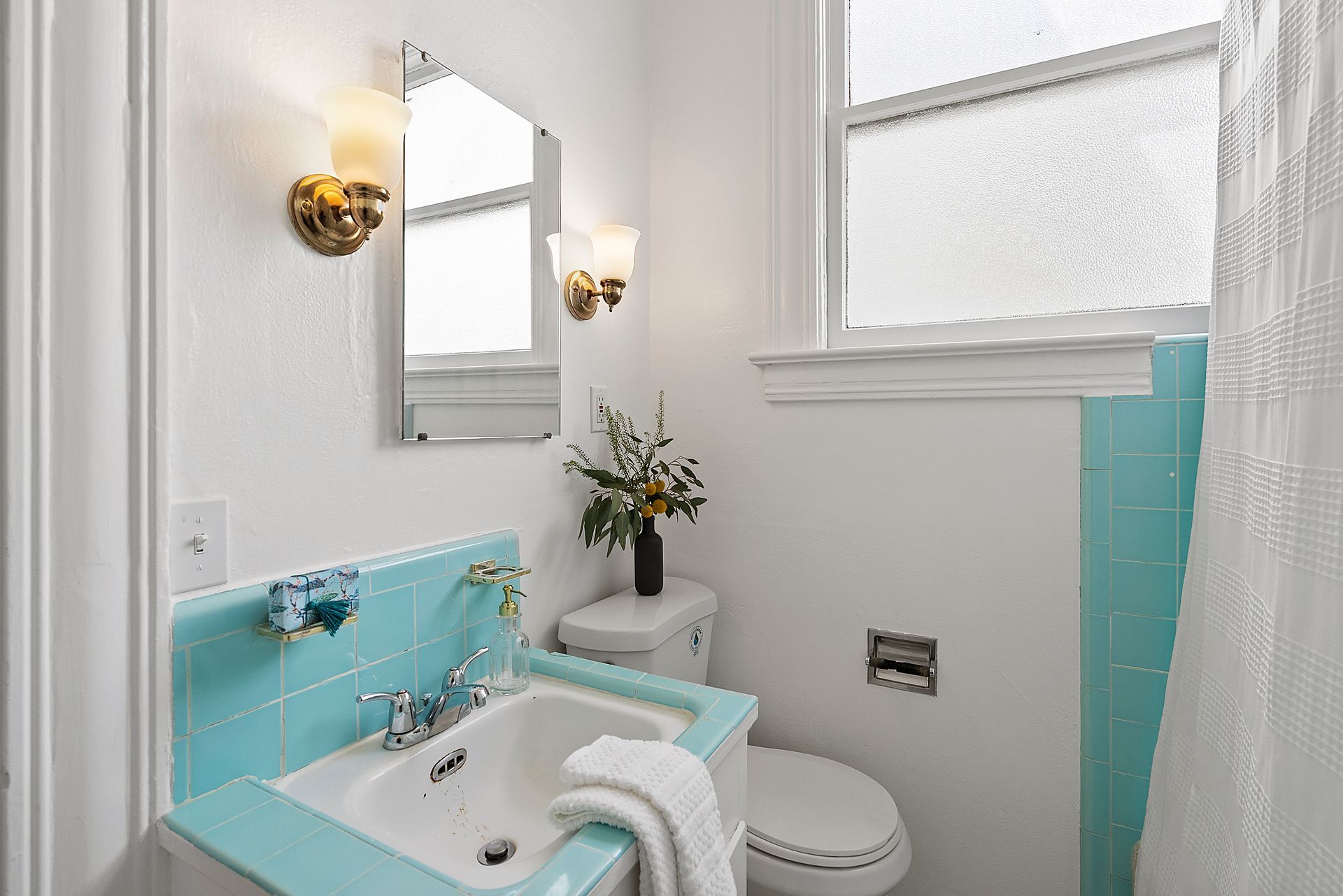 A bathroom with a sink , toilet , mirror and window.