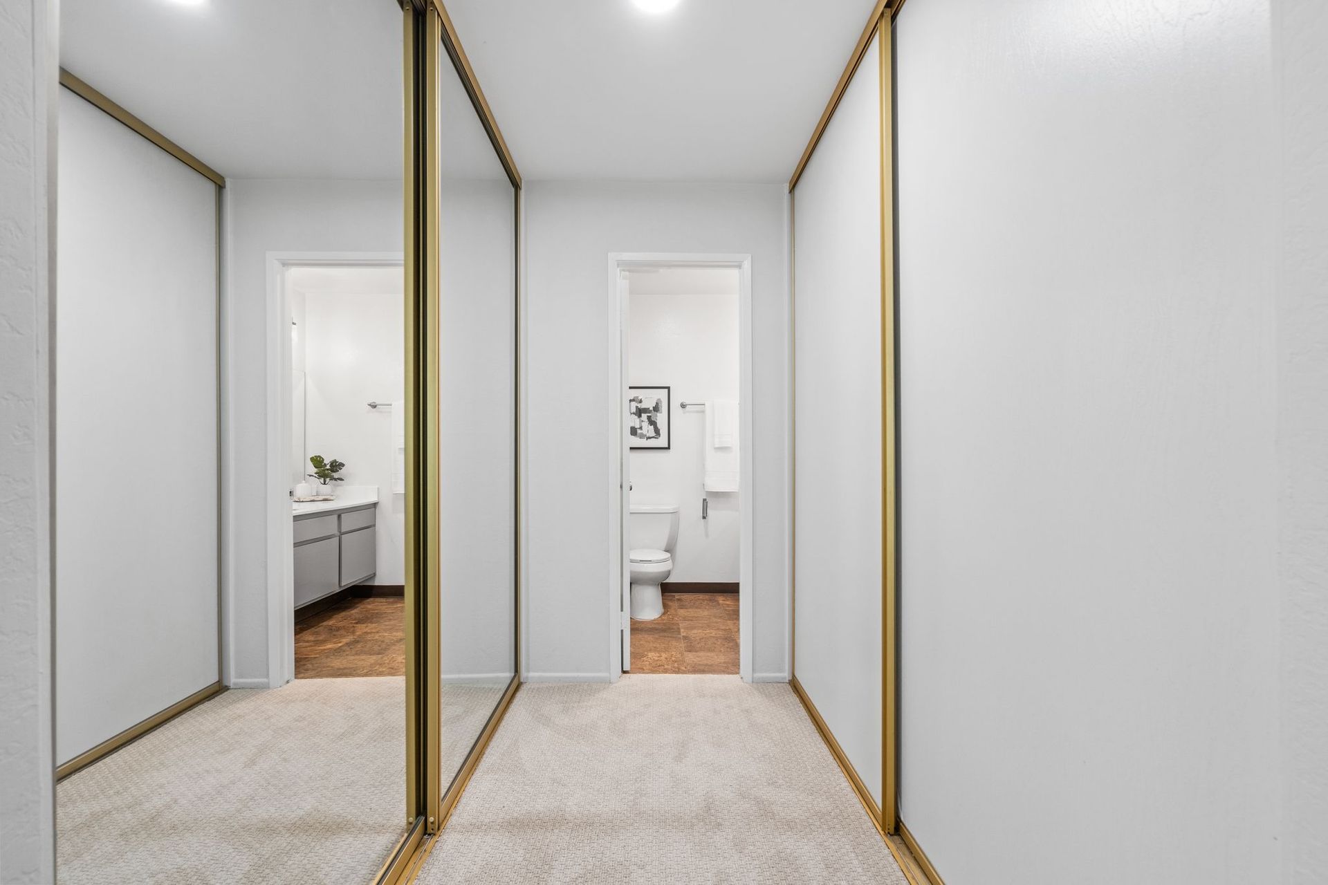 A hallway with sliding mirrored doors leading to a bathroom.