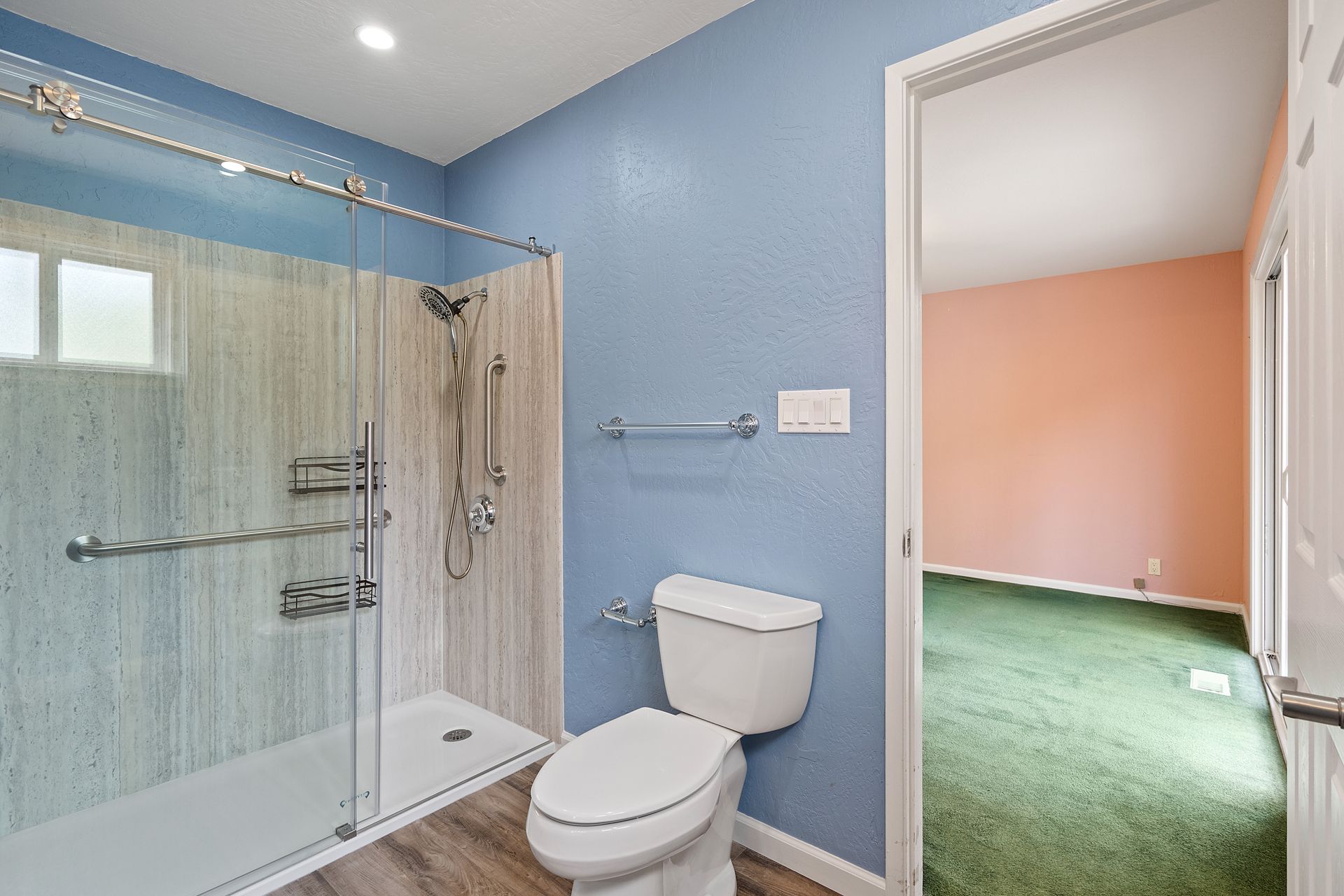 A bathroom with a toilet , shower and sliding glass door.